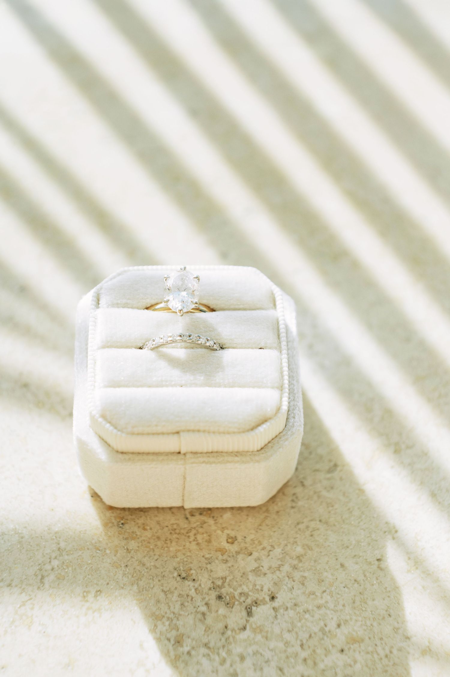 Wedding rings displayed in a white ring box with diagonal light and shadow patterns.