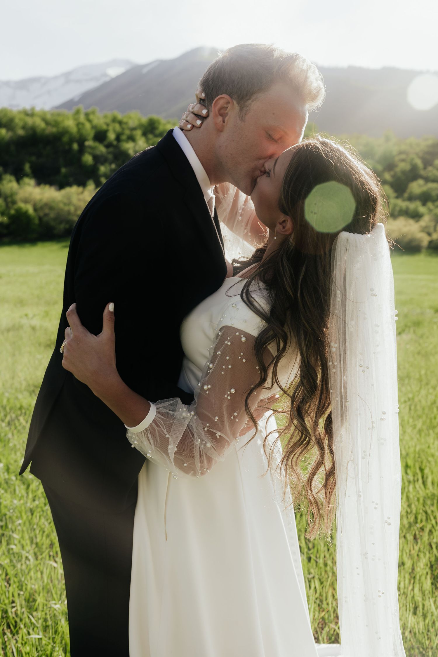 A romantic wedding moment captured in golden sunlight with mountains in the background.