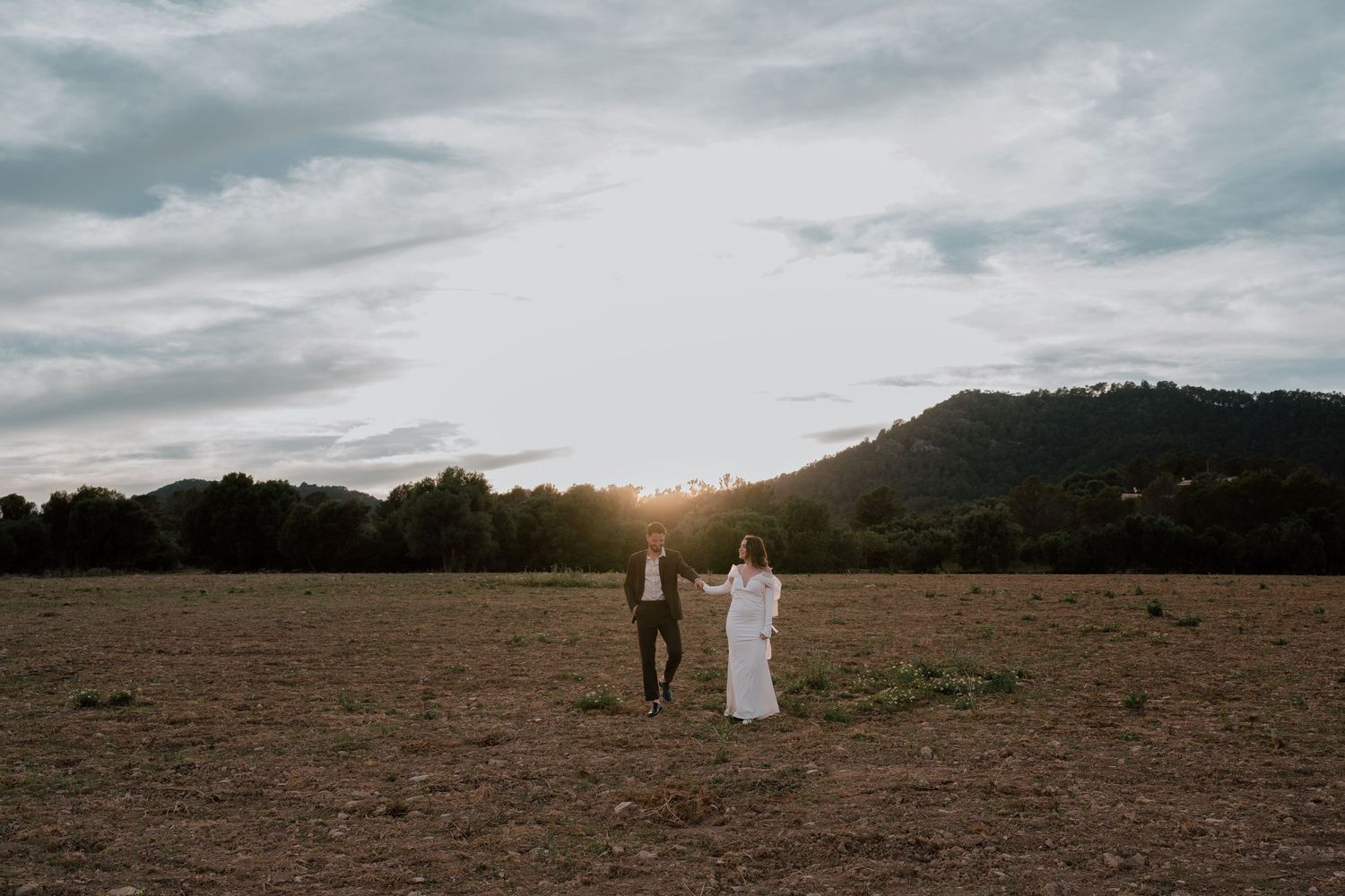 A distant couple stands in a vast field under dramatic cloudy skies.