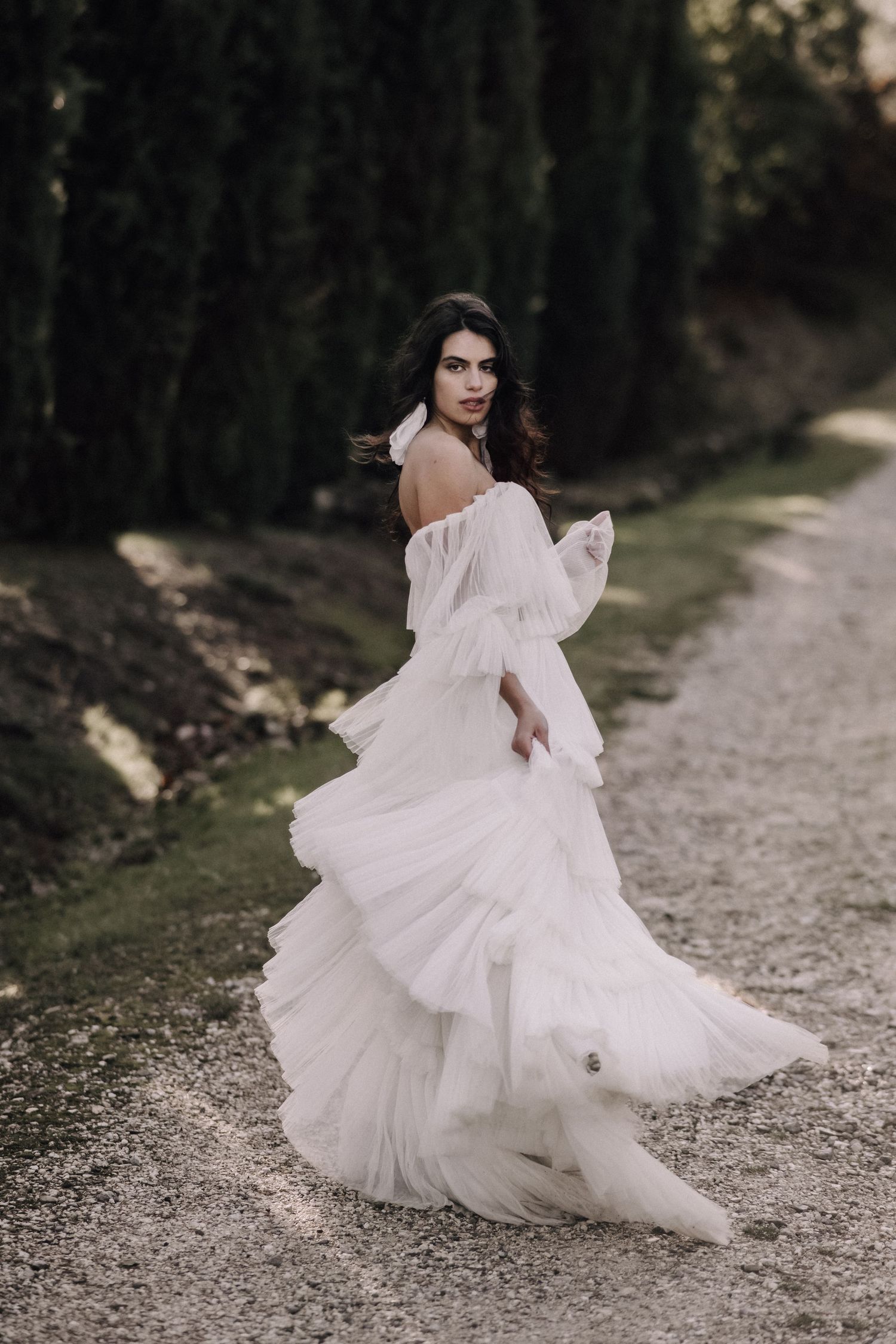 A flowing white wedding dress twirls dramatically on a forest path.