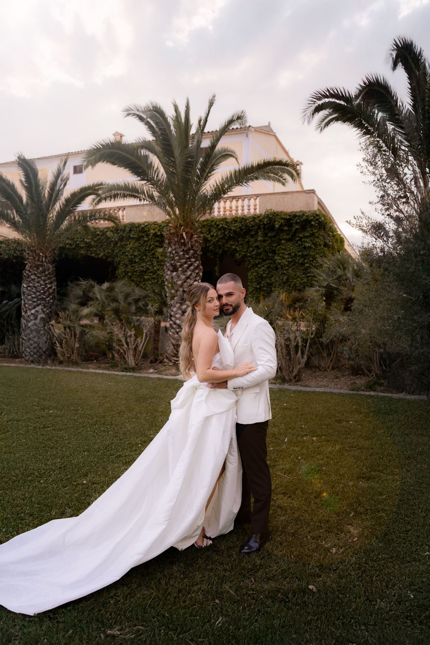 A romantic sequence in a garden setting with a couple in white attire against palm trees.