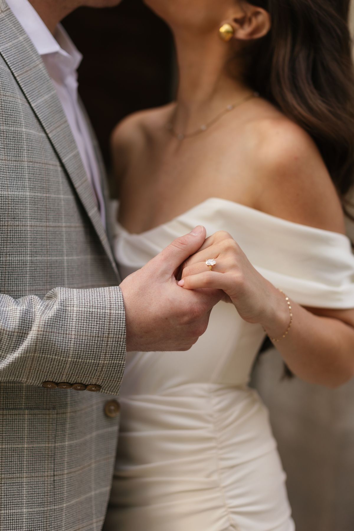 Close-up of hands clasped together with glimpses of a white dress and gray suit.