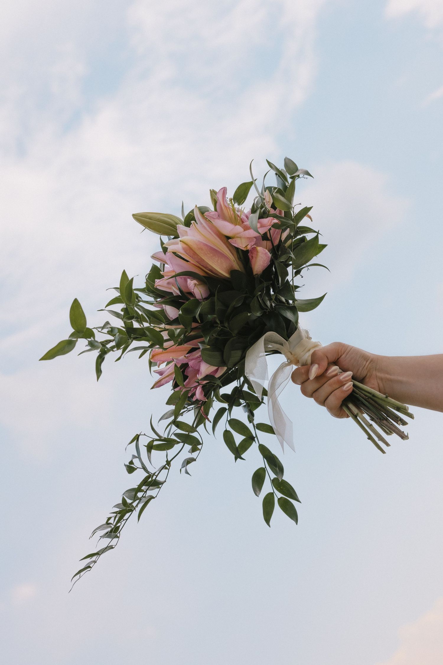 A hand holding a vibrant pink and green floral bouquet against a bright blue sky.