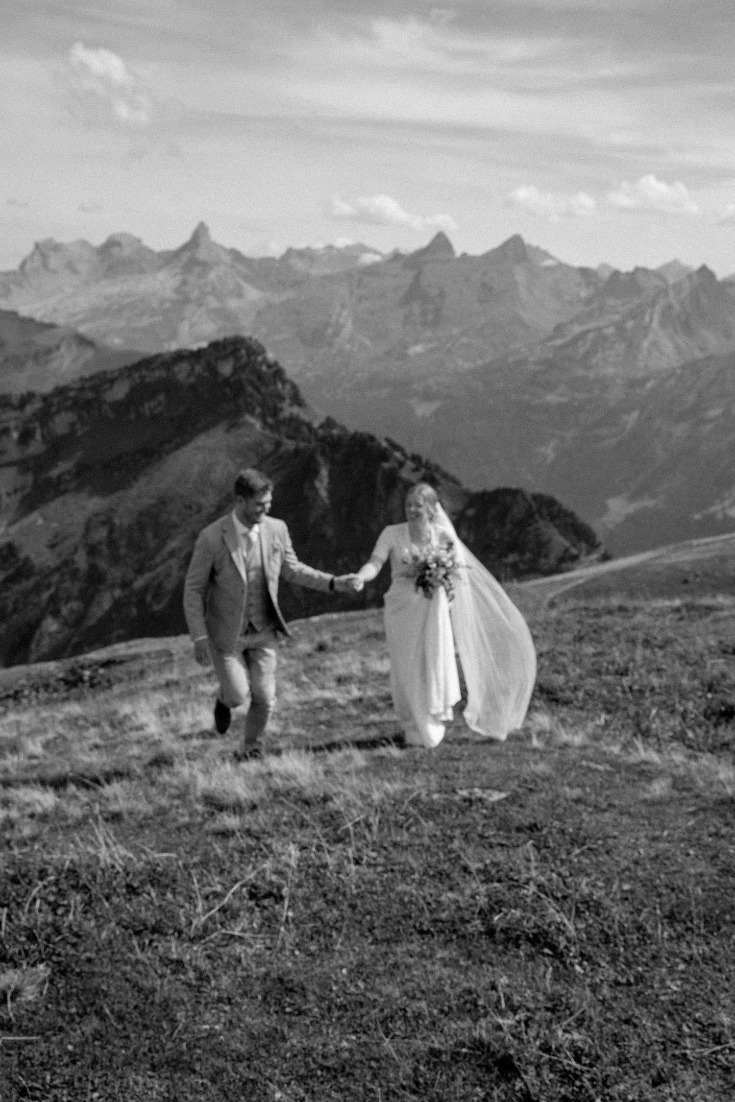 A wedding couple poses against dramatic mountain peaks in black and white photography.