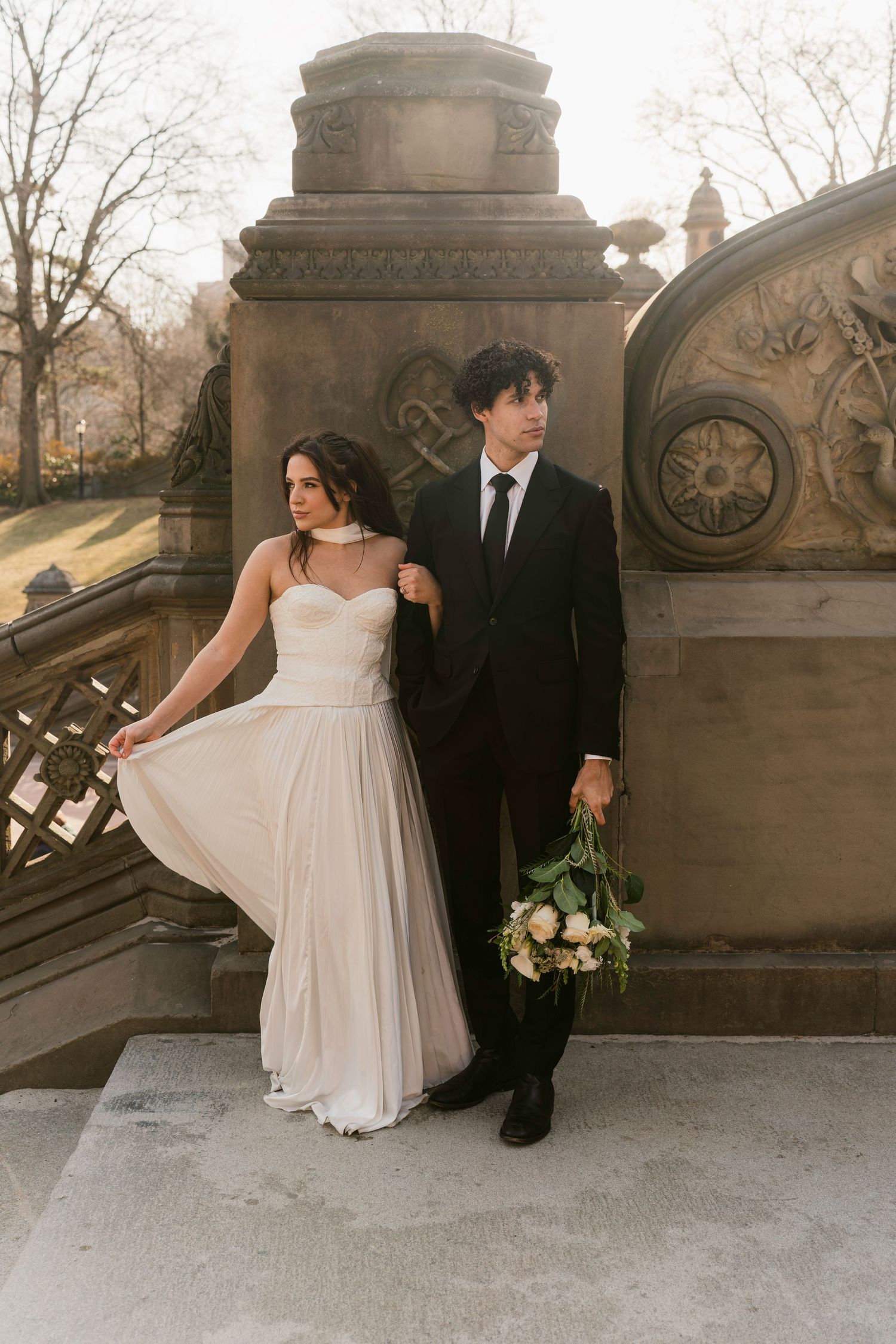 Elegant wedding couple posing on ornate stone bridge in classic architectural setting.