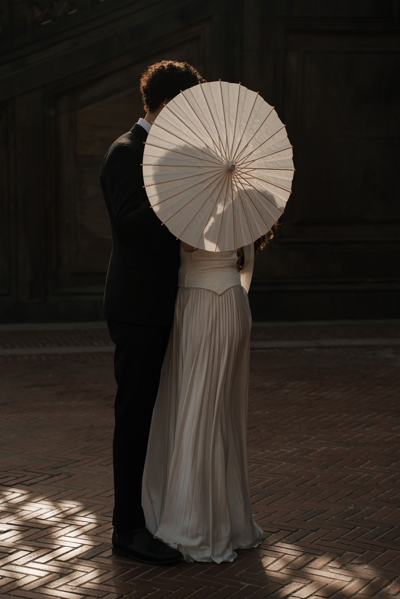 Dramatic silhouettes of a couple with white parasols in low lighting.