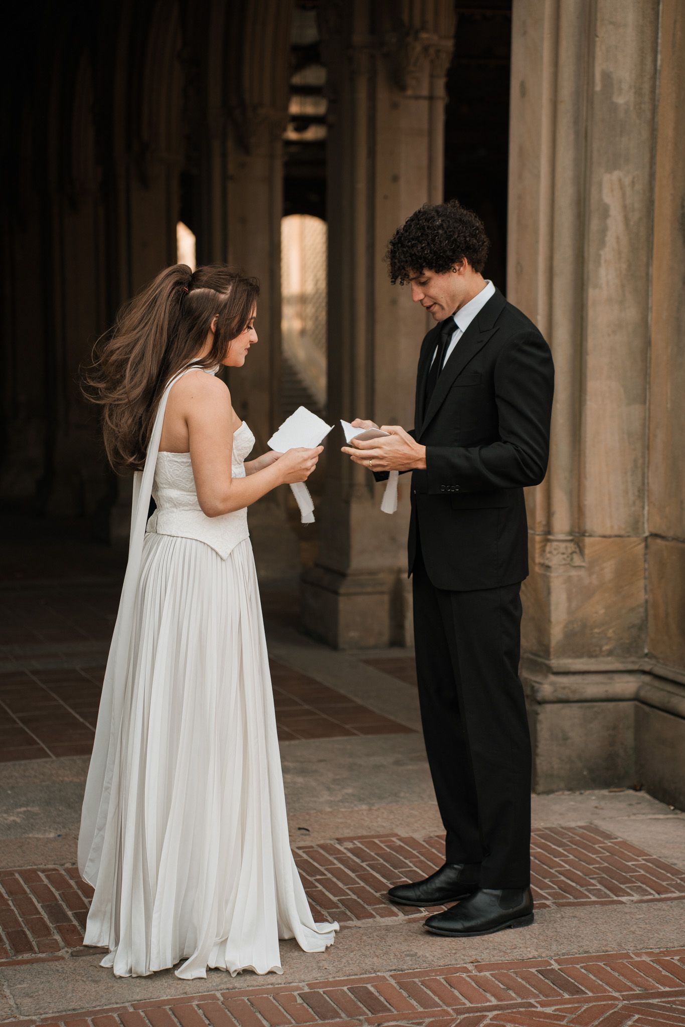 A couple in wedding attire stands on brick pavement exchanging private moments.