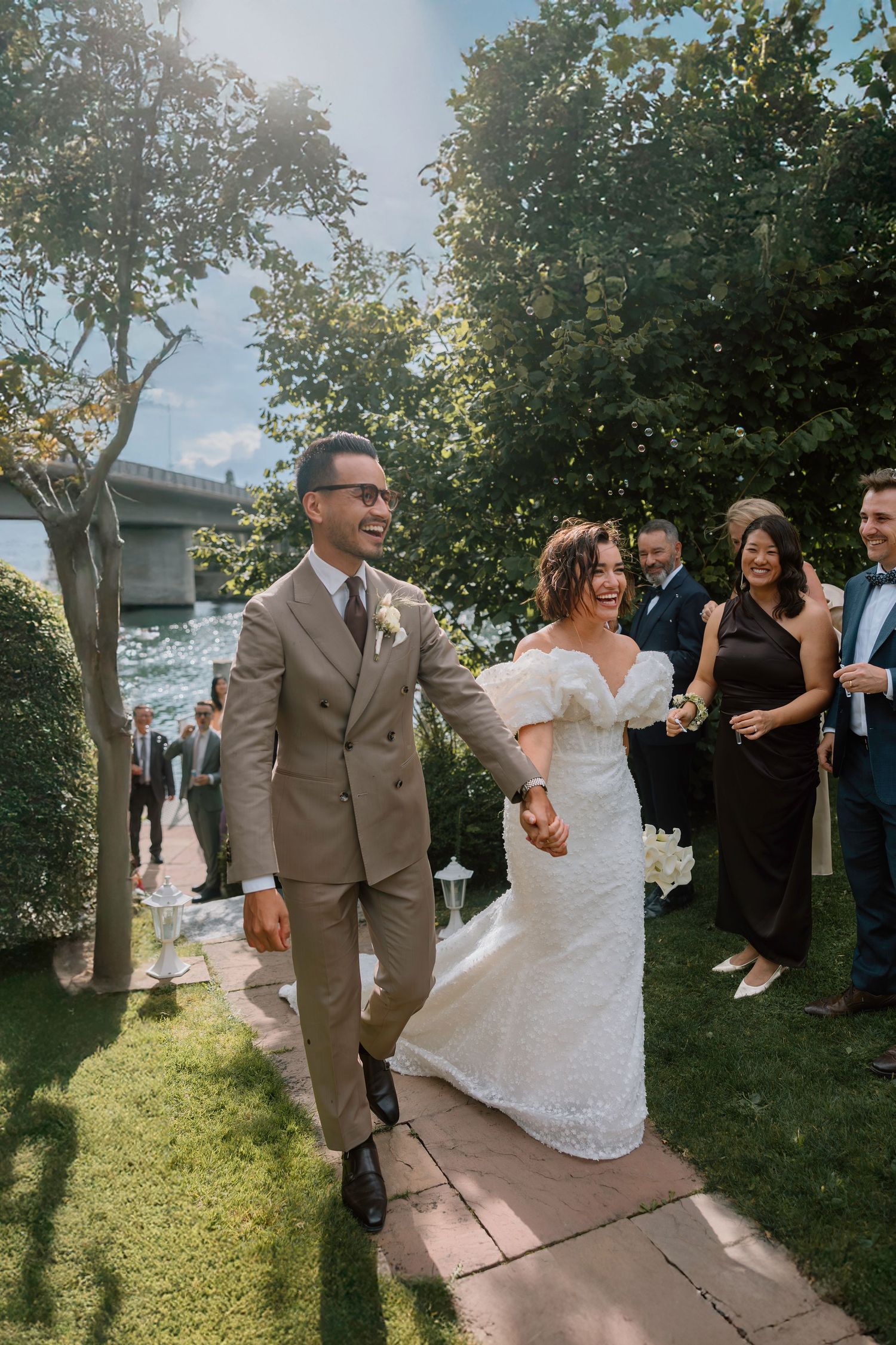 Wedding couple walking joyfully on outdoor path while guests watch and celebrate.