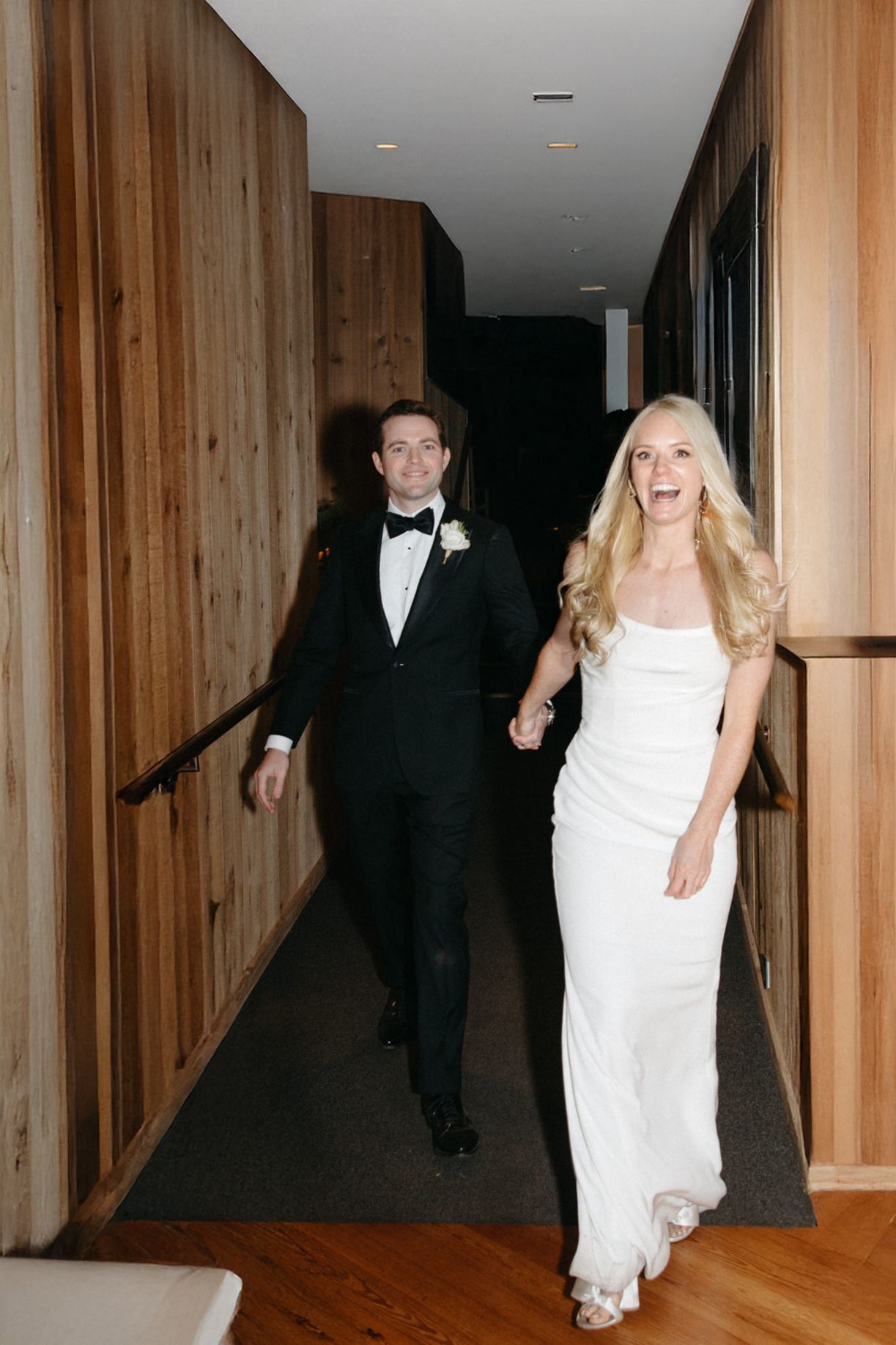 A couple walking down a modern hallway with wood paneled walls.