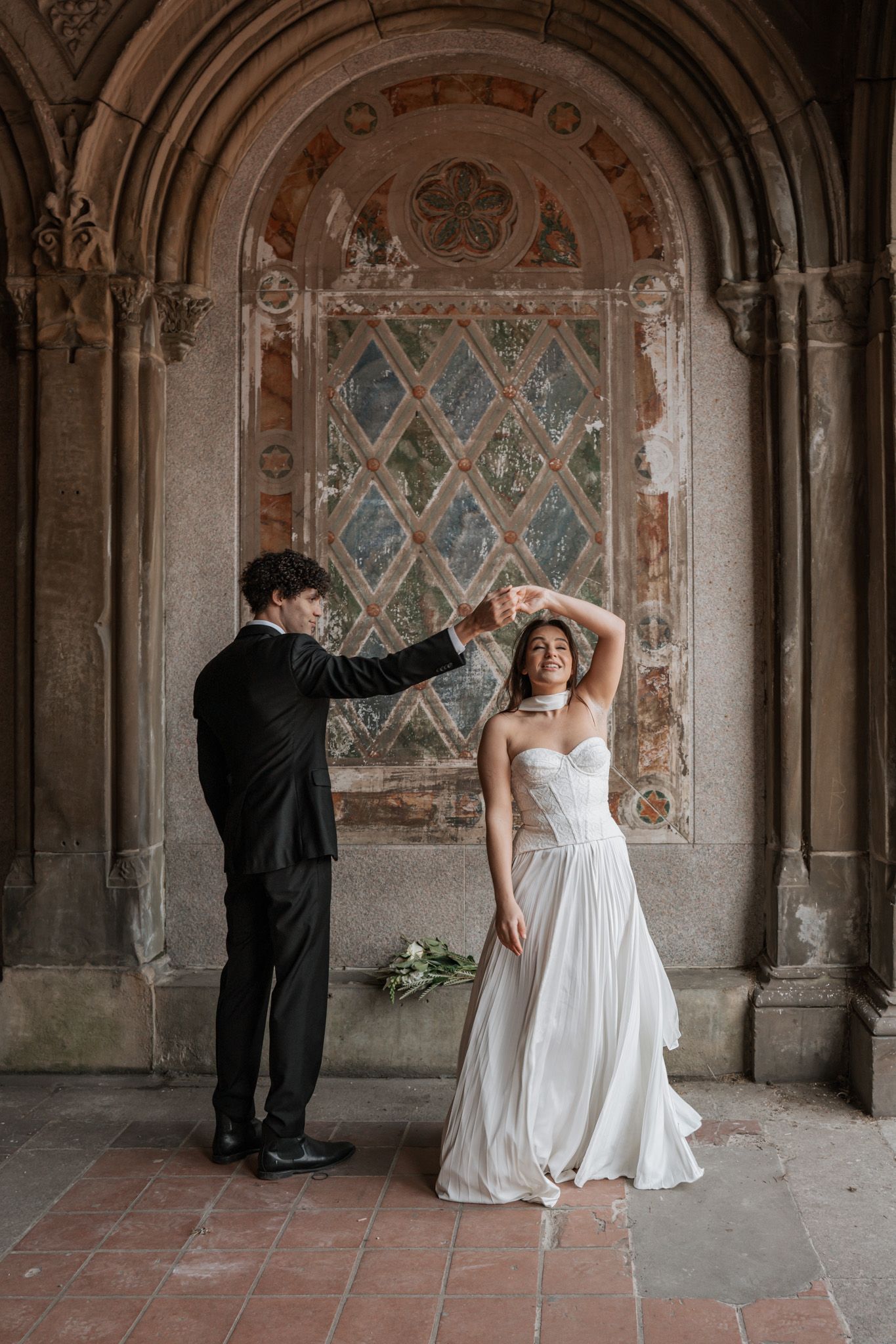 Wedding couple dances in historic stone archway with decorative wall paintings.