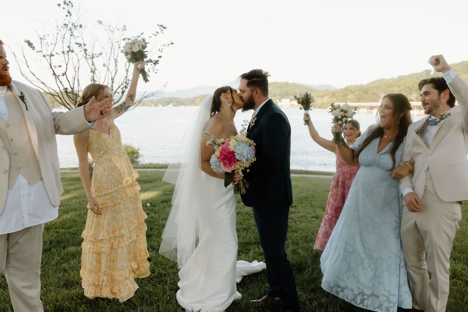 Wedding guests celebrate and dance outdoors against a scenic mountain backdrop.