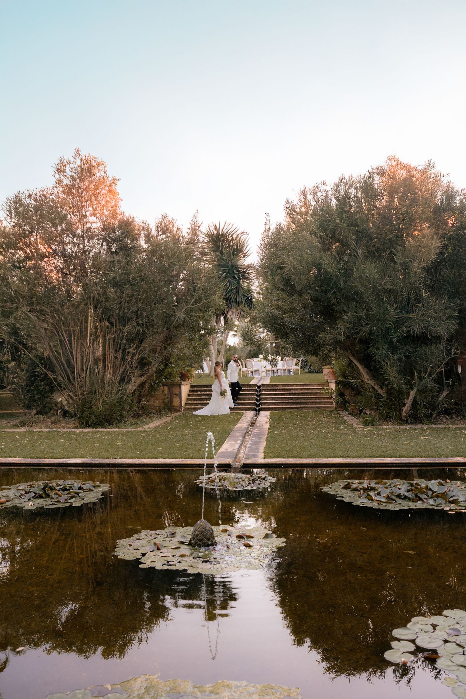 Scenic wedding photos by a reflective pond with lily pads and steps in the background.