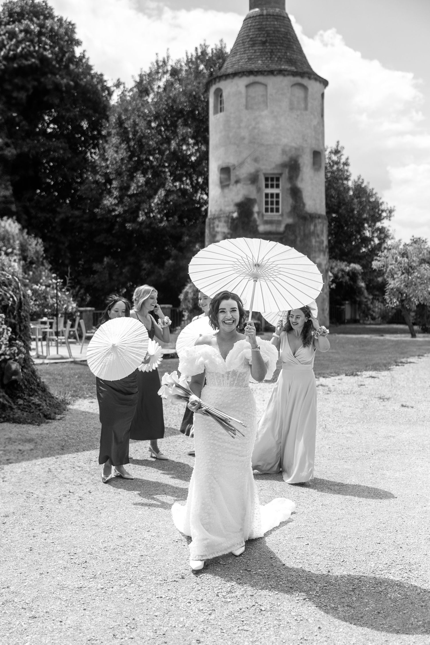 Wedding celebration with white parasols outside historic stone building.