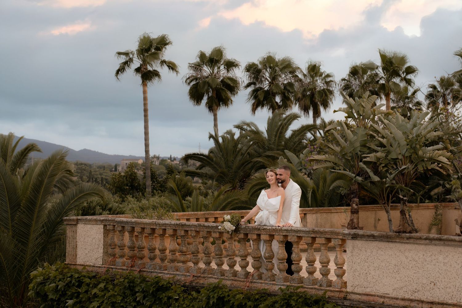 Elegant outdoor wedding venue with palm trees and stone balustrades at sunset.