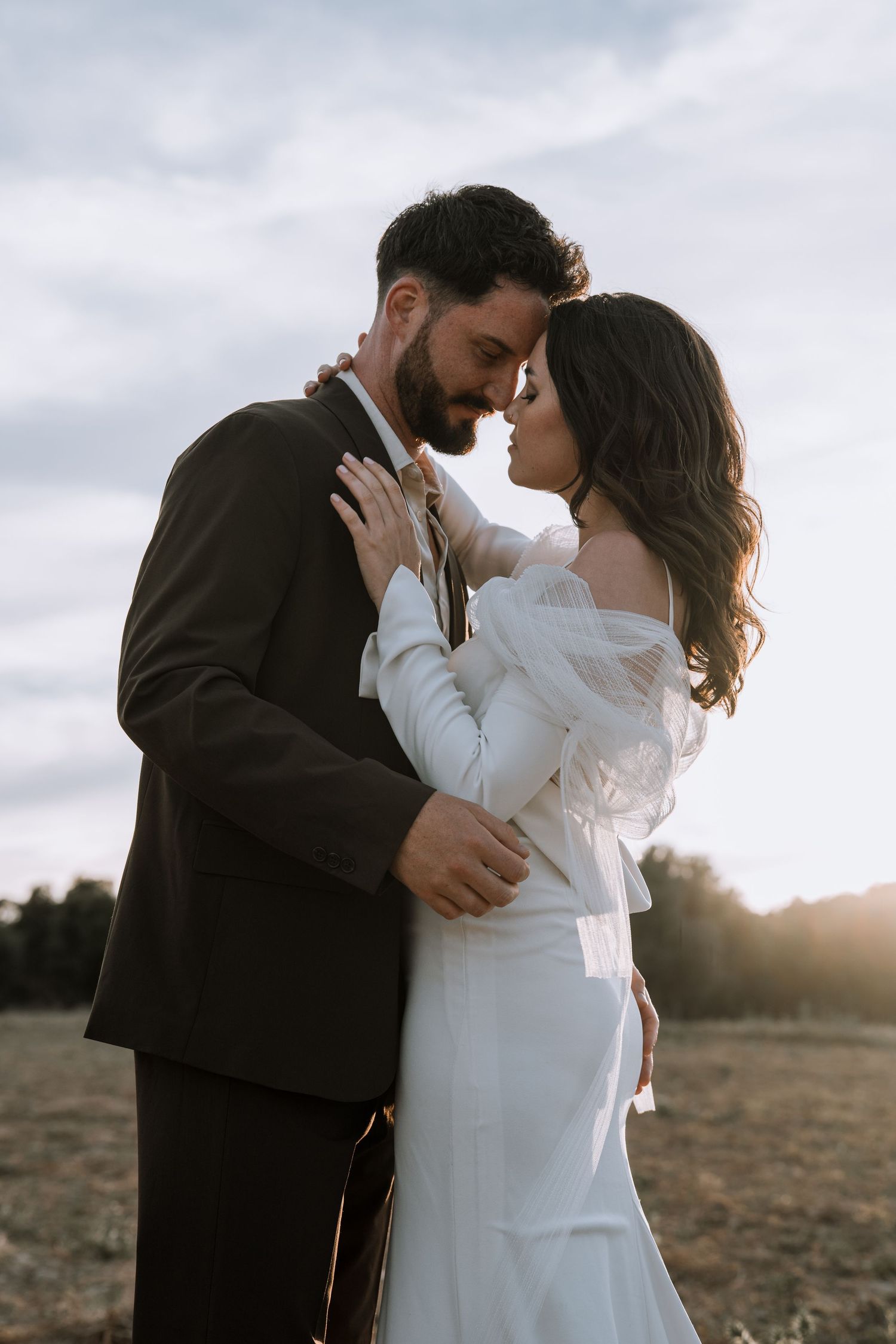 A couple embraces in soft natural light during their wedding photoshoot in an outdoor setting.