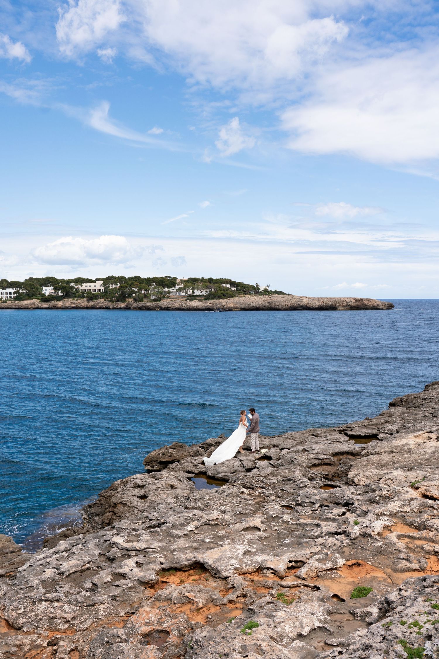 Rocky coastal landscape with bright blue Mediterranean waters and distant cliffs under a sunny sky.