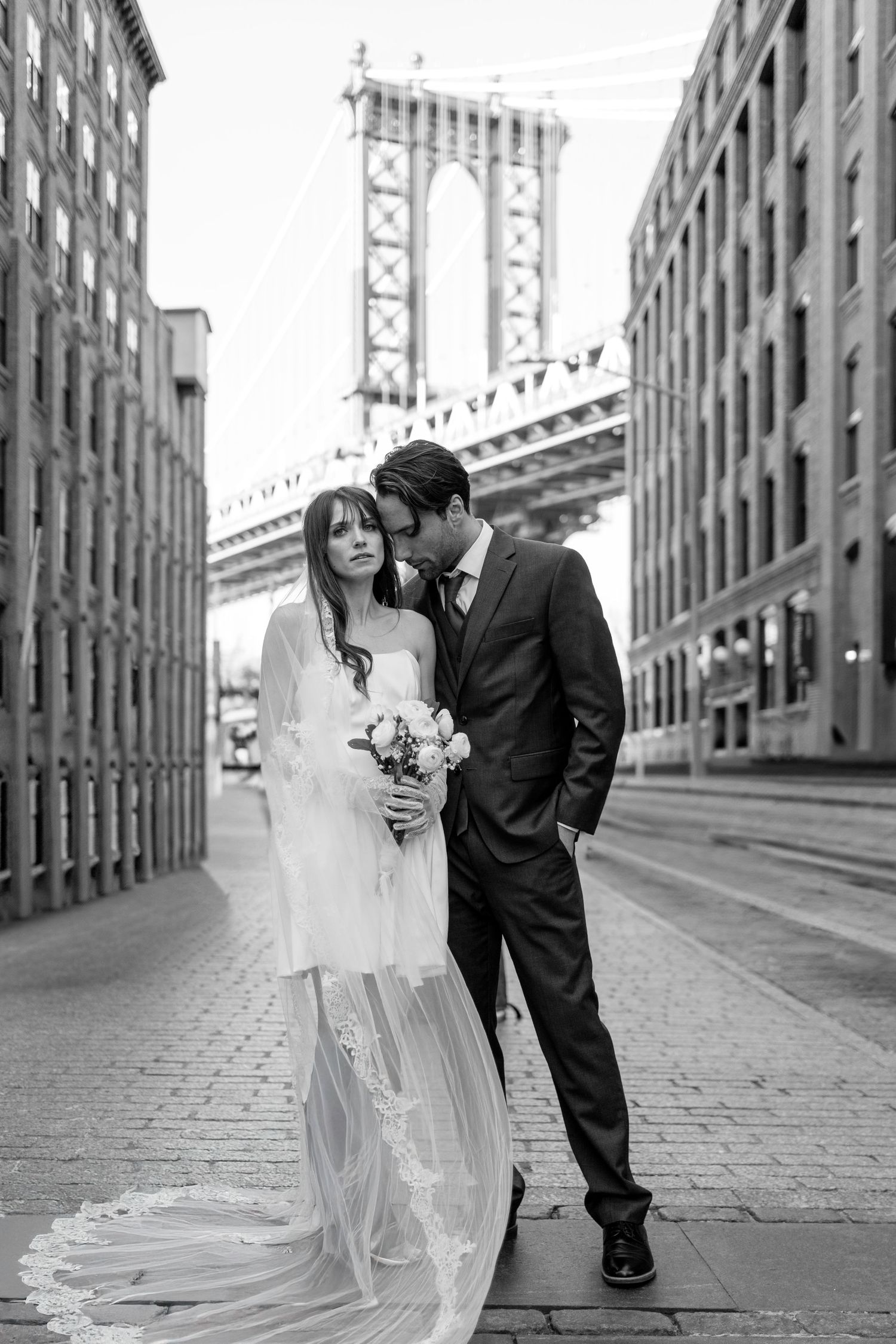 Black and white wedding photos taken on a cobblestone street with industrial architecture.