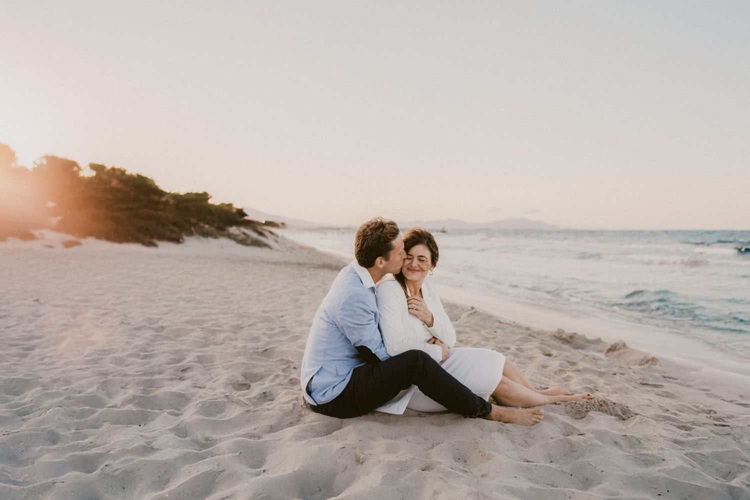 Couple enjoying a romantic moment on a sandy beach at sunset.