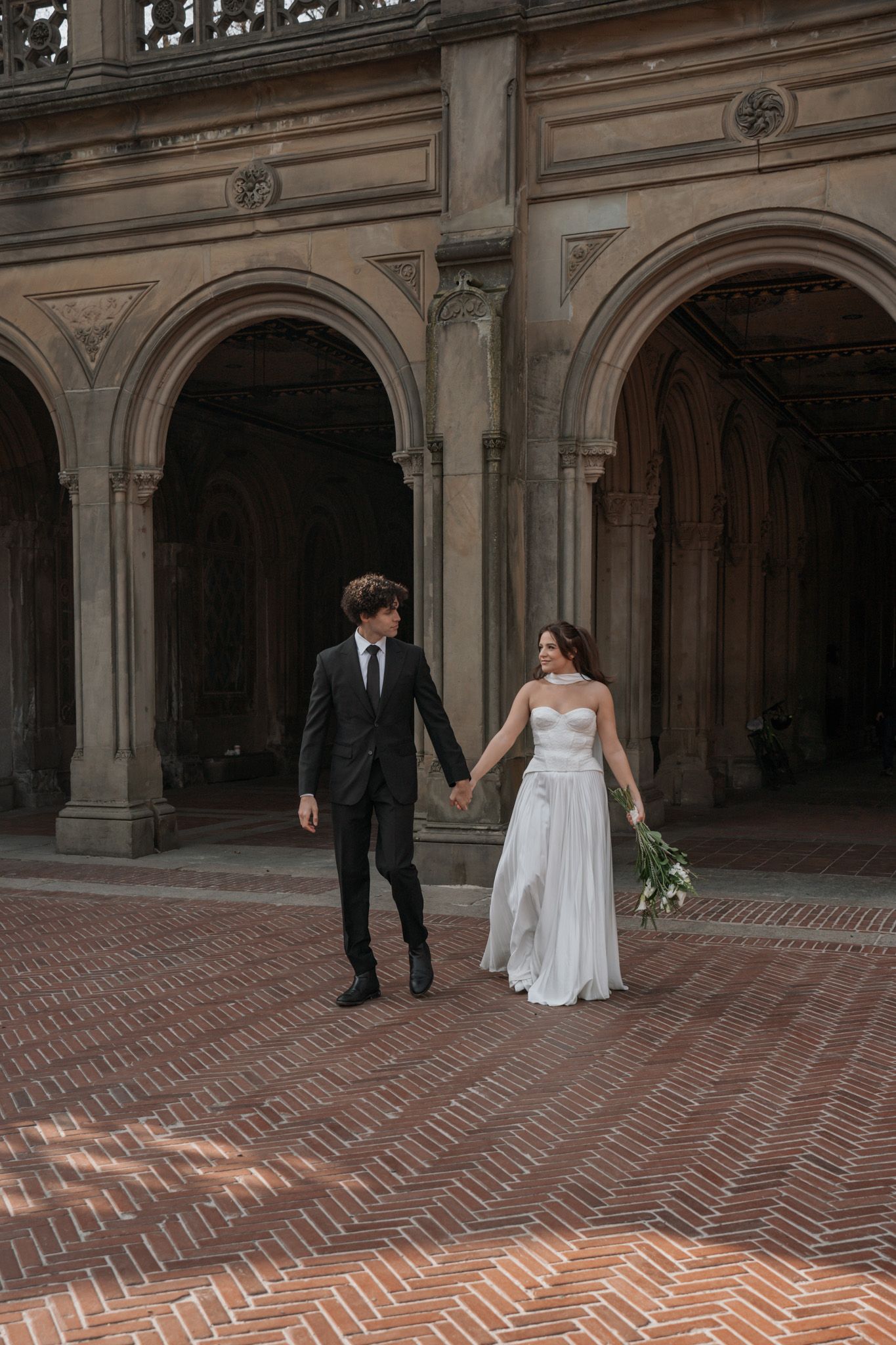 Couple dances across brick-paved courtyard beneath historic stone archways.