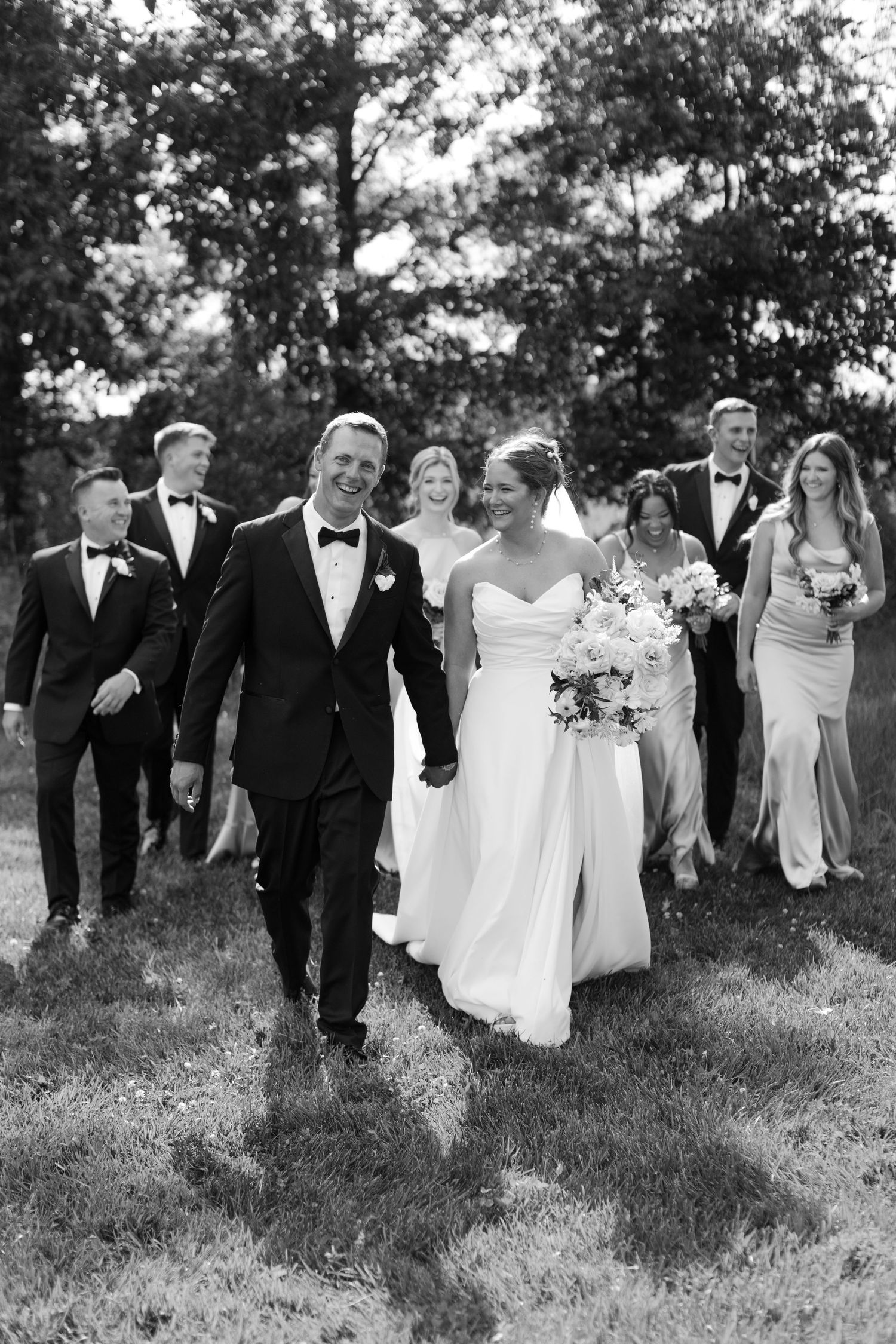 A wedding party walking through a grassy field in black and white.