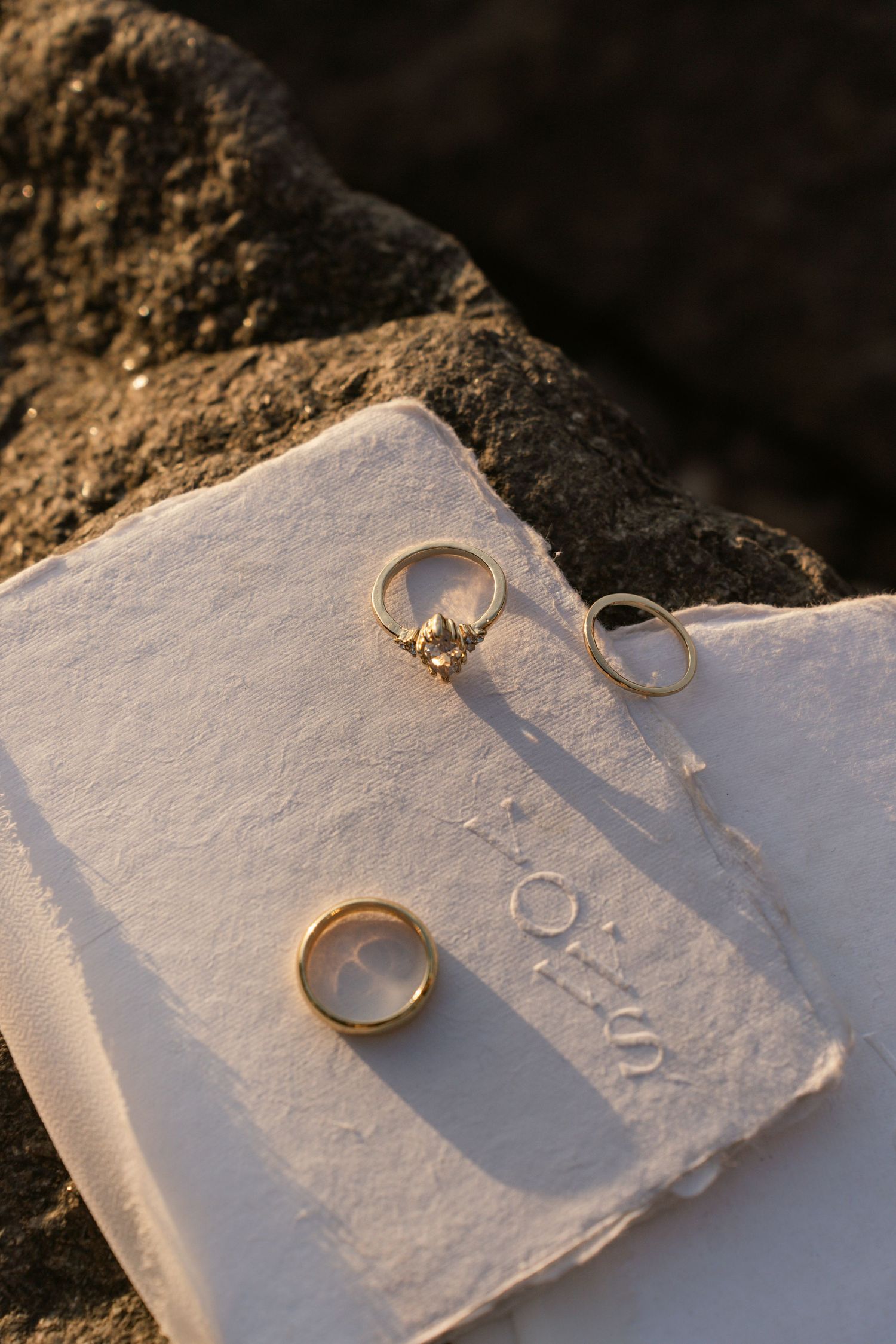 Wedding rings photographed on textured white paper in natural sunlight.