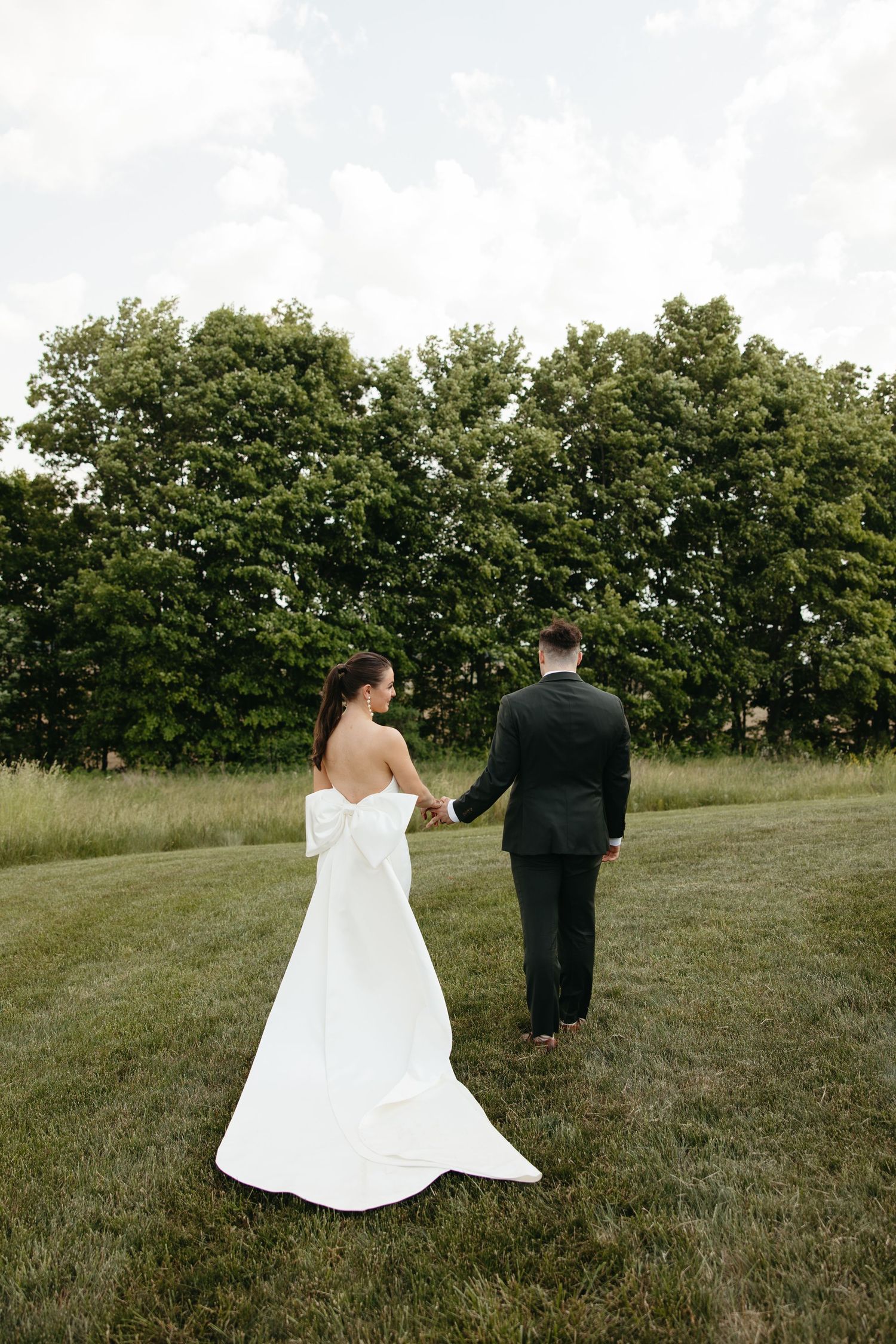 A couple walks through a grassy field on their wedding day.