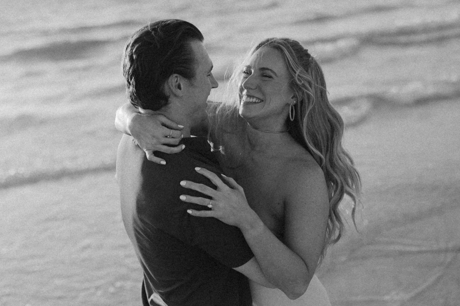 Couple embracing and laughing together on a sandy beach at sunset.