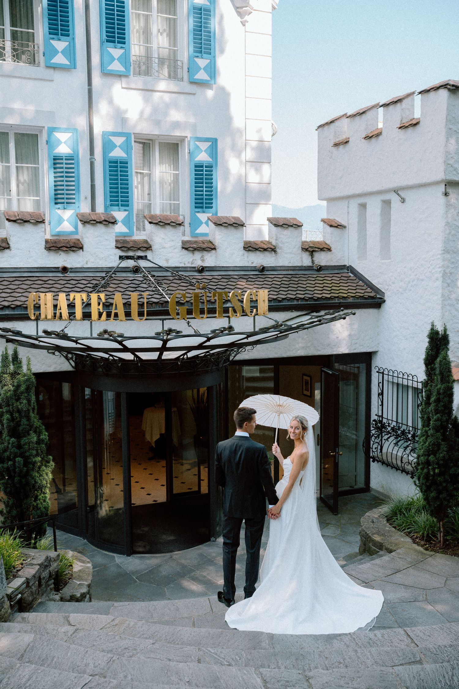 A wedding couple poses outside a white building with blue shutters and modern architecture.
