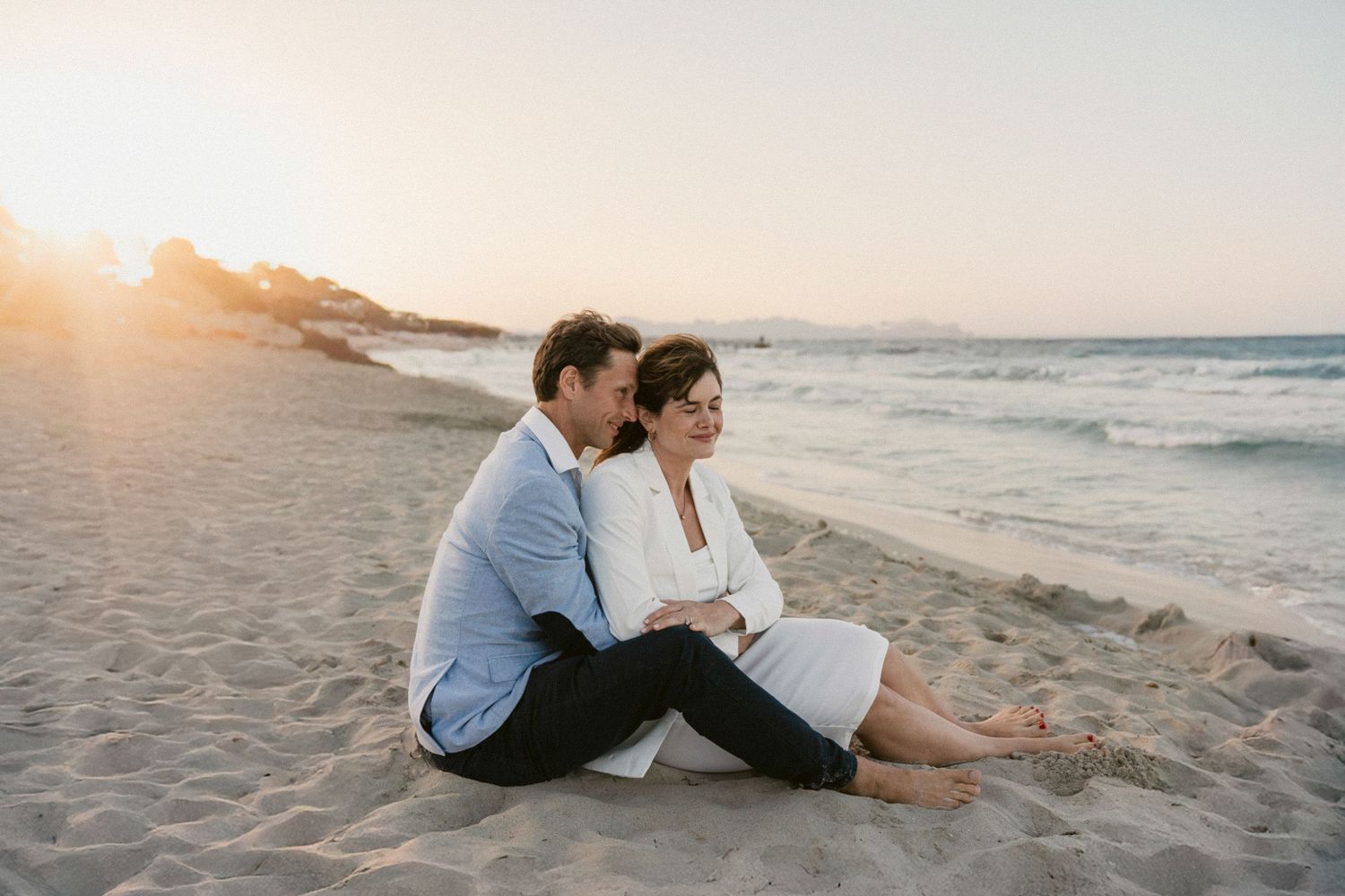 Couple walking and sitting together on sandy beach during golden hour.