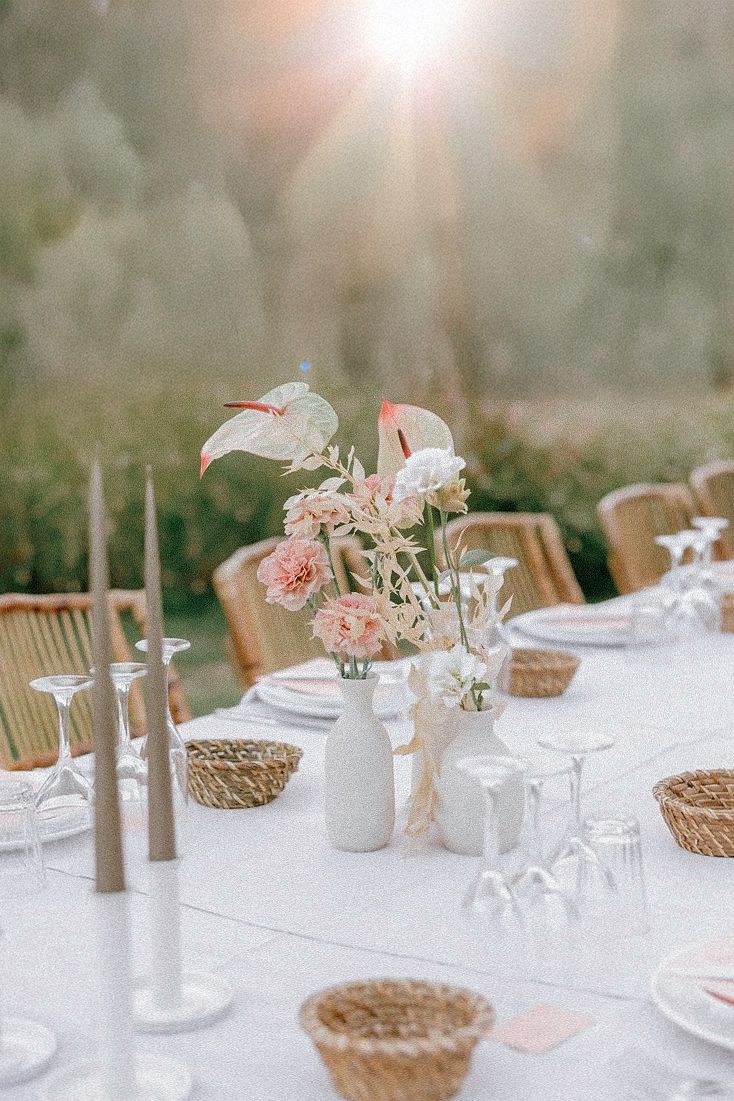 Elegant wedding table setting with white linens, woven basket accents, soft pink floral centerpieces and tapered candles.
