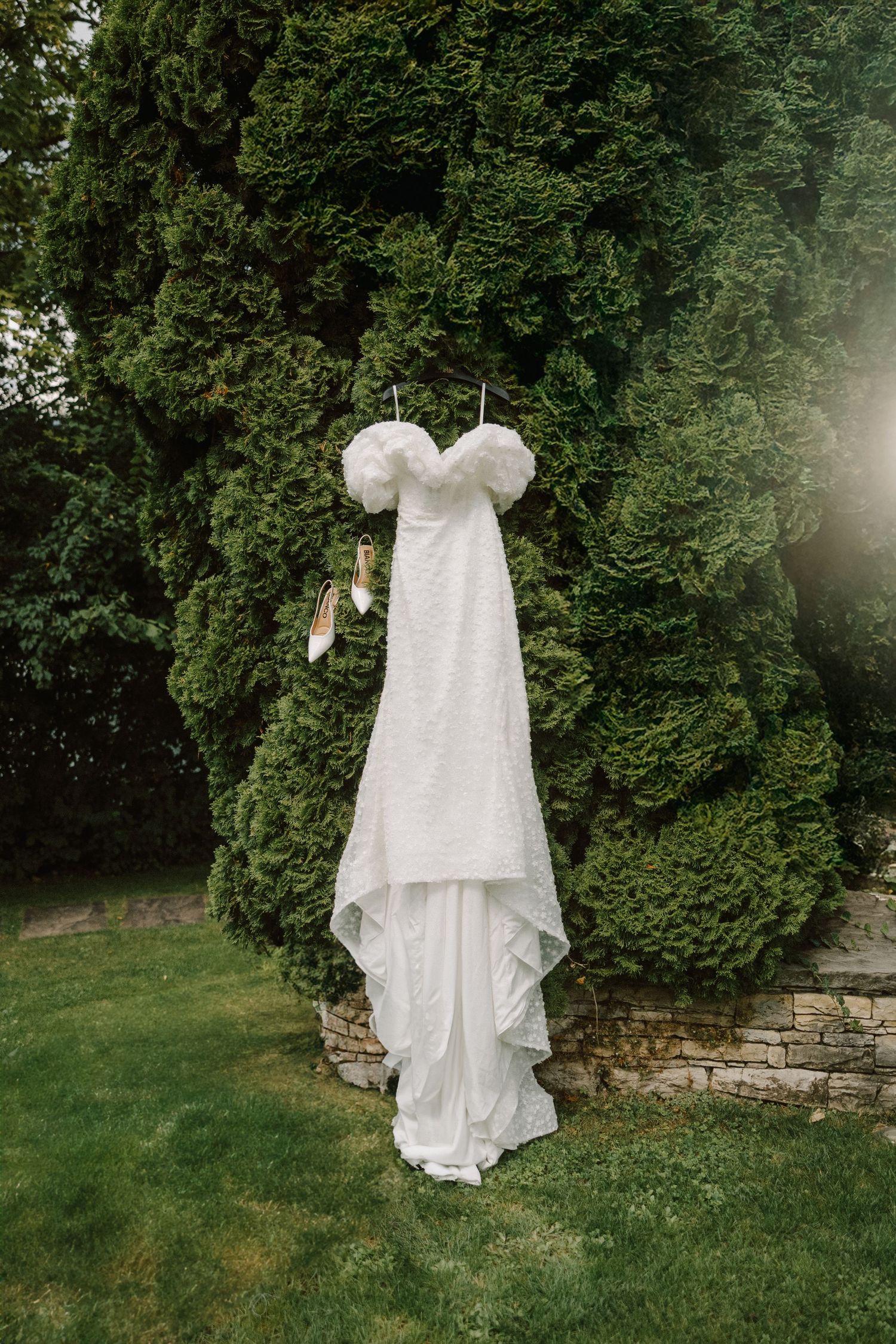 White wedding dress hanging against green garden foliage.