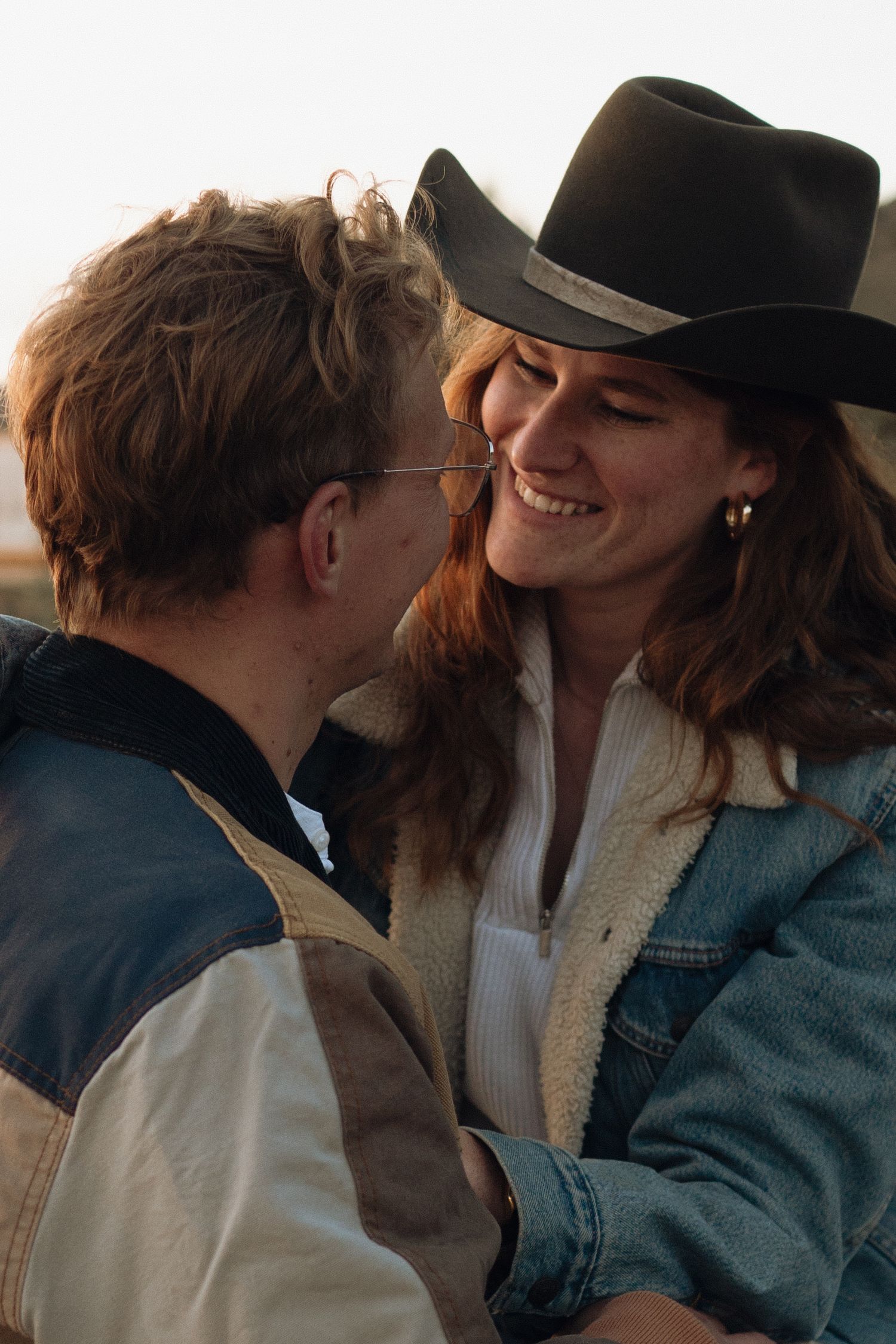 Intimate moment shared between two people wearing casual denim and hats against a bright background.