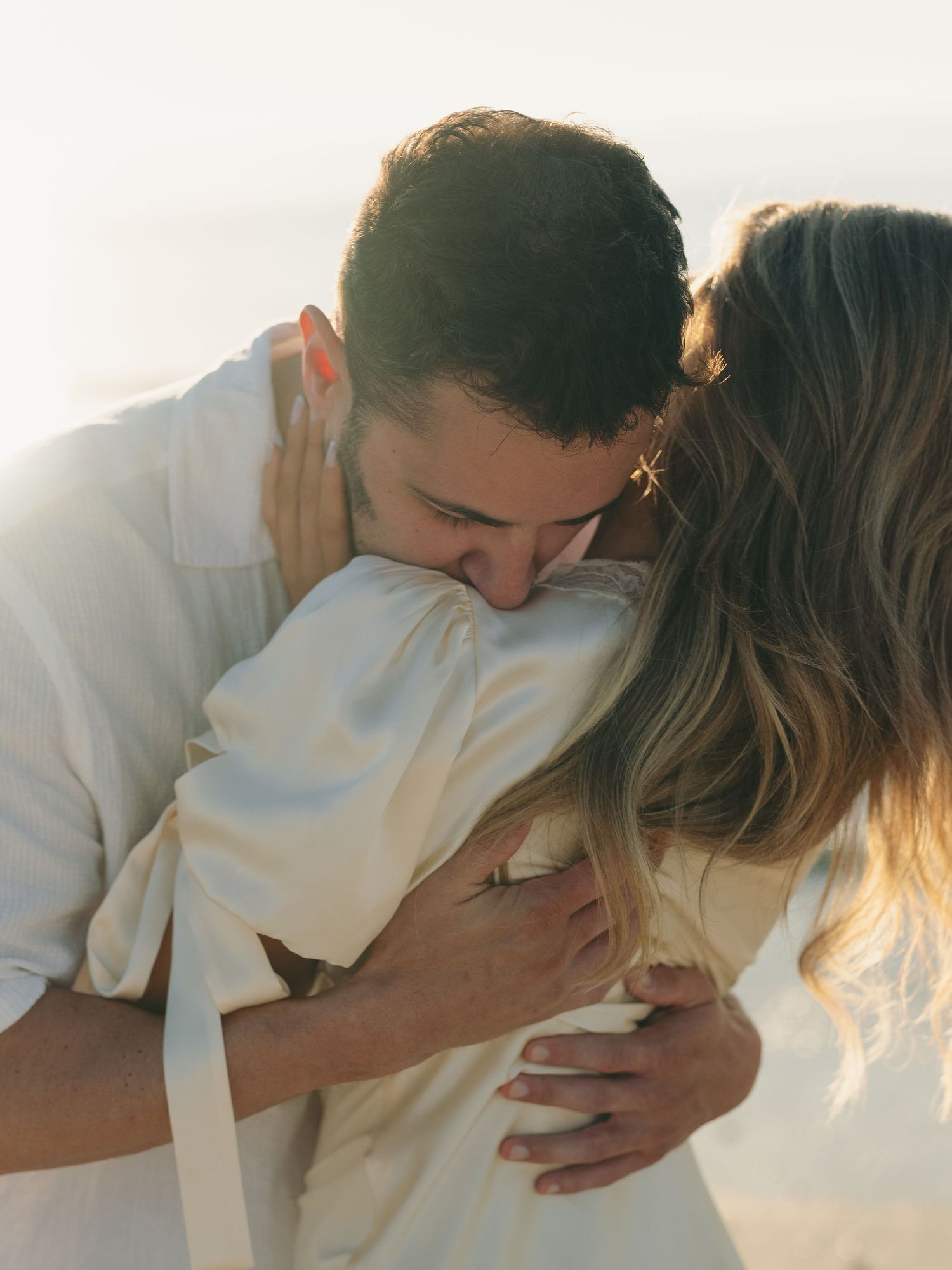 Romantic couple embracing and kissing in dreamy sunlit beach setting.