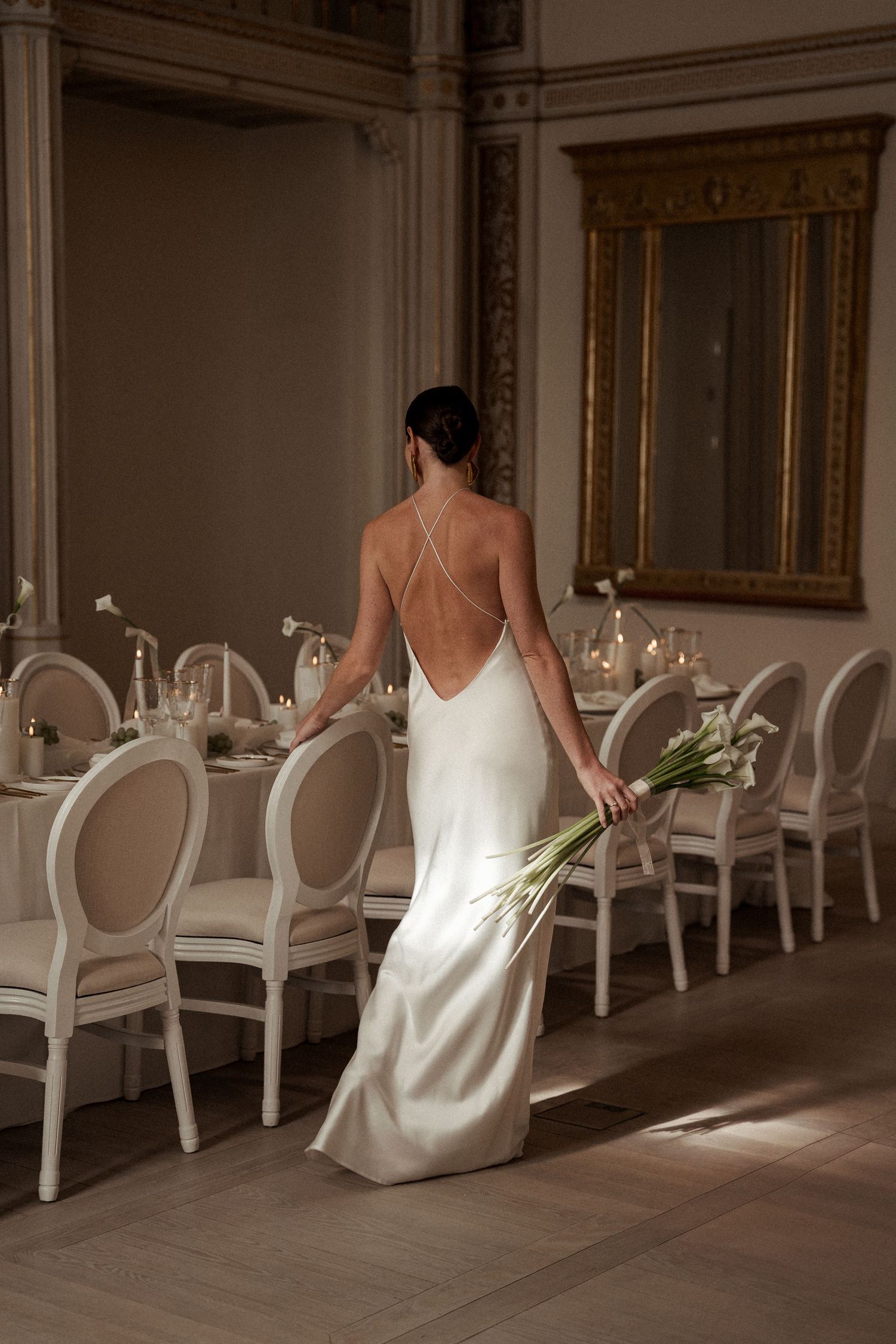 Elegant figure in white dress walking through luxurious dining room with ornate chairs.