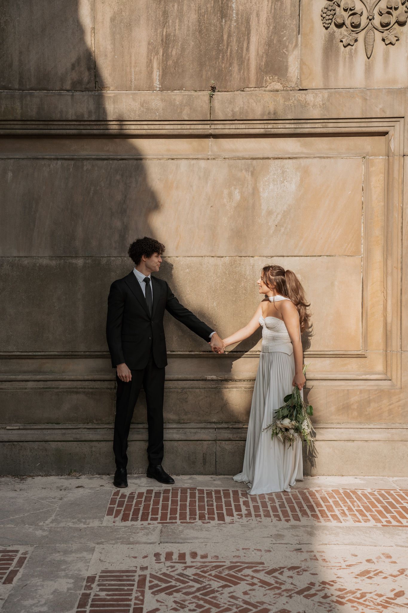Wedding couple performs playful dance moves along stone wall and brick floor.