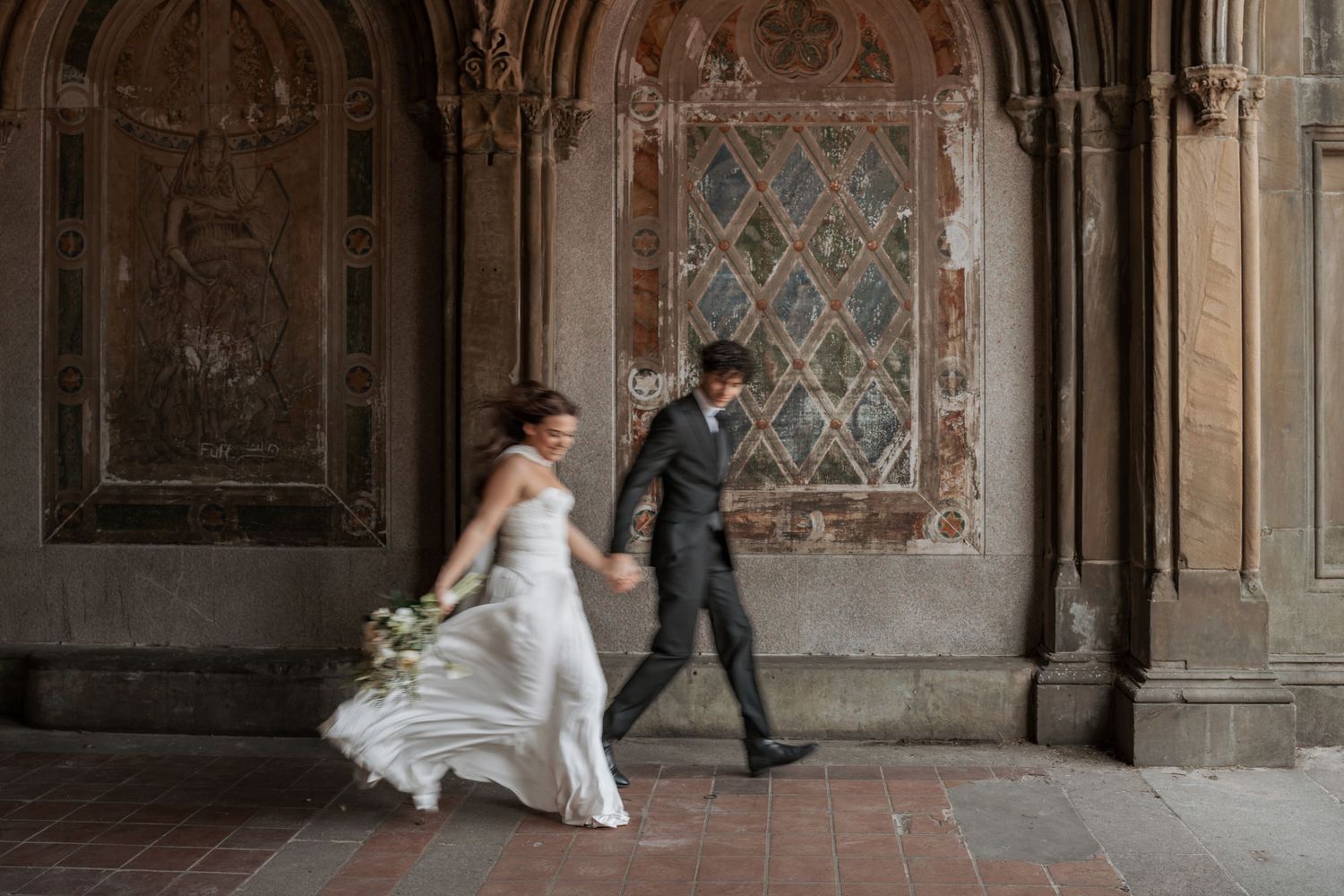 Wedding party poses for photos in an ornate stone church archway.