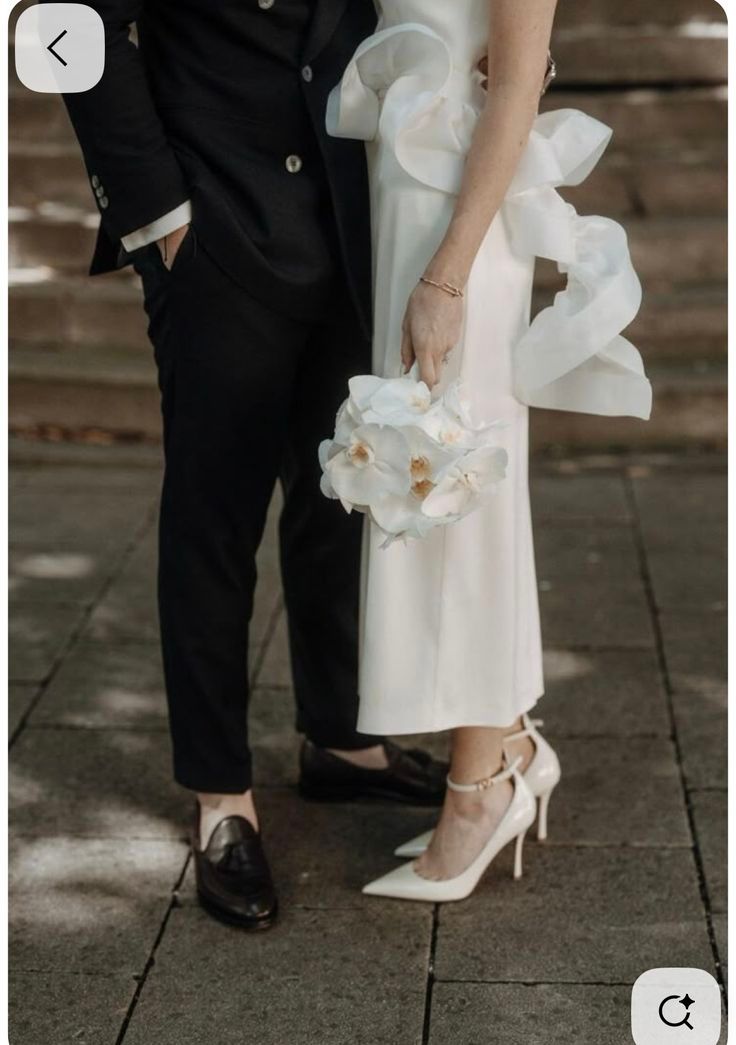 Close-up of elegant white bridal shoes and dress hem against dark stone pavement.