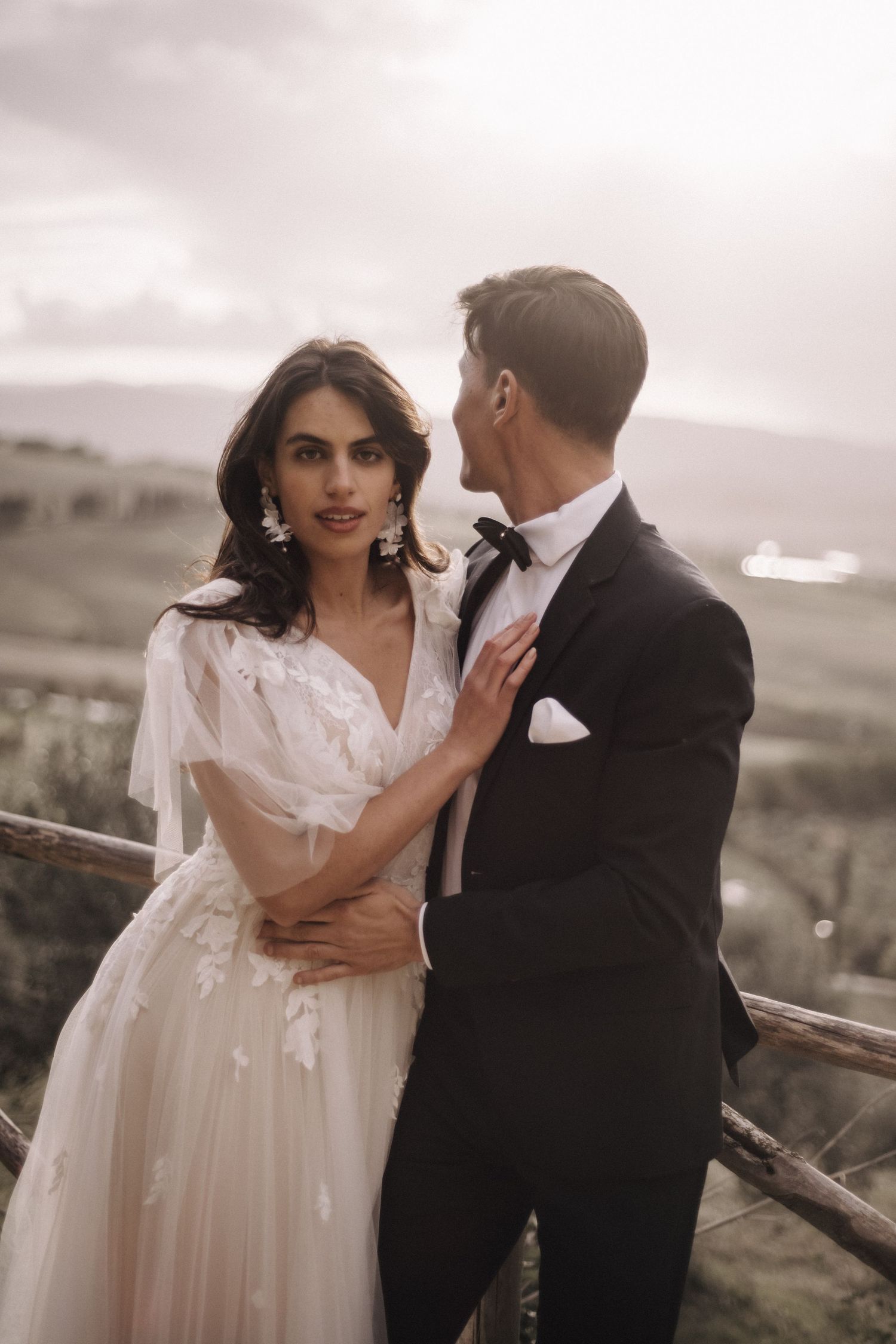 A romantic wedding moment captured against a moody sky with dramatic lighting.