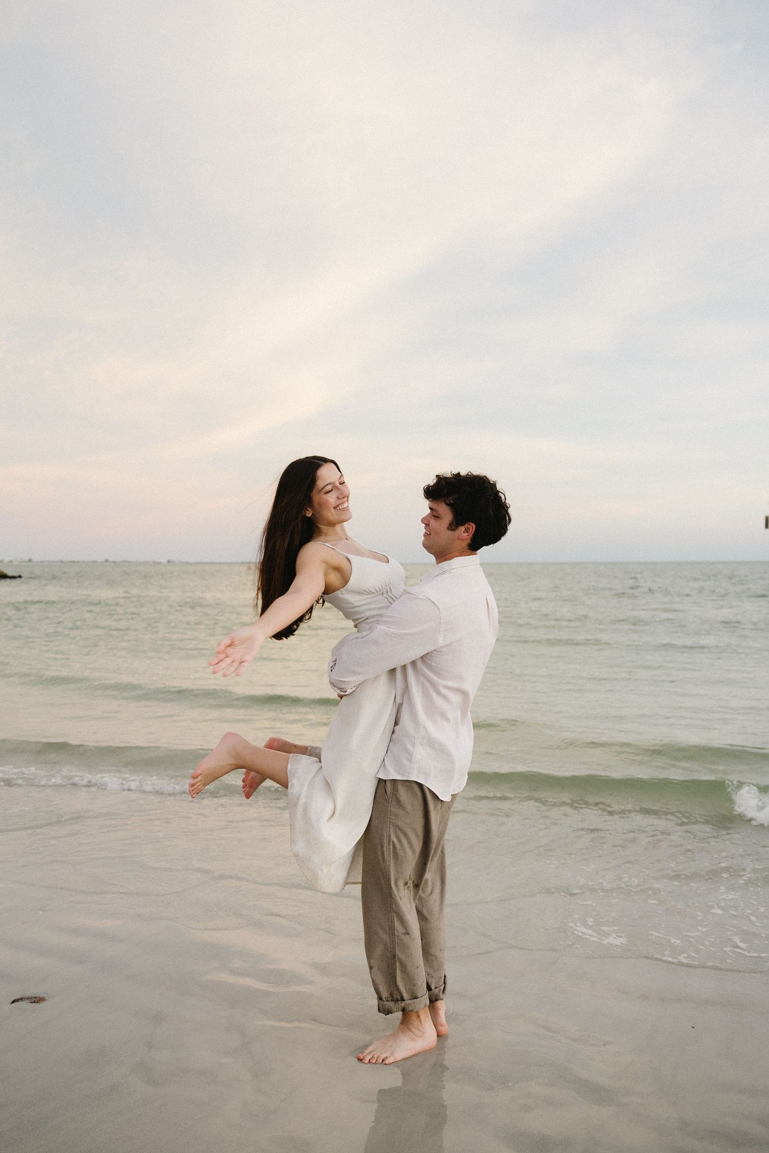 Couple embracing and dancing together on a serene beach at sunset.
