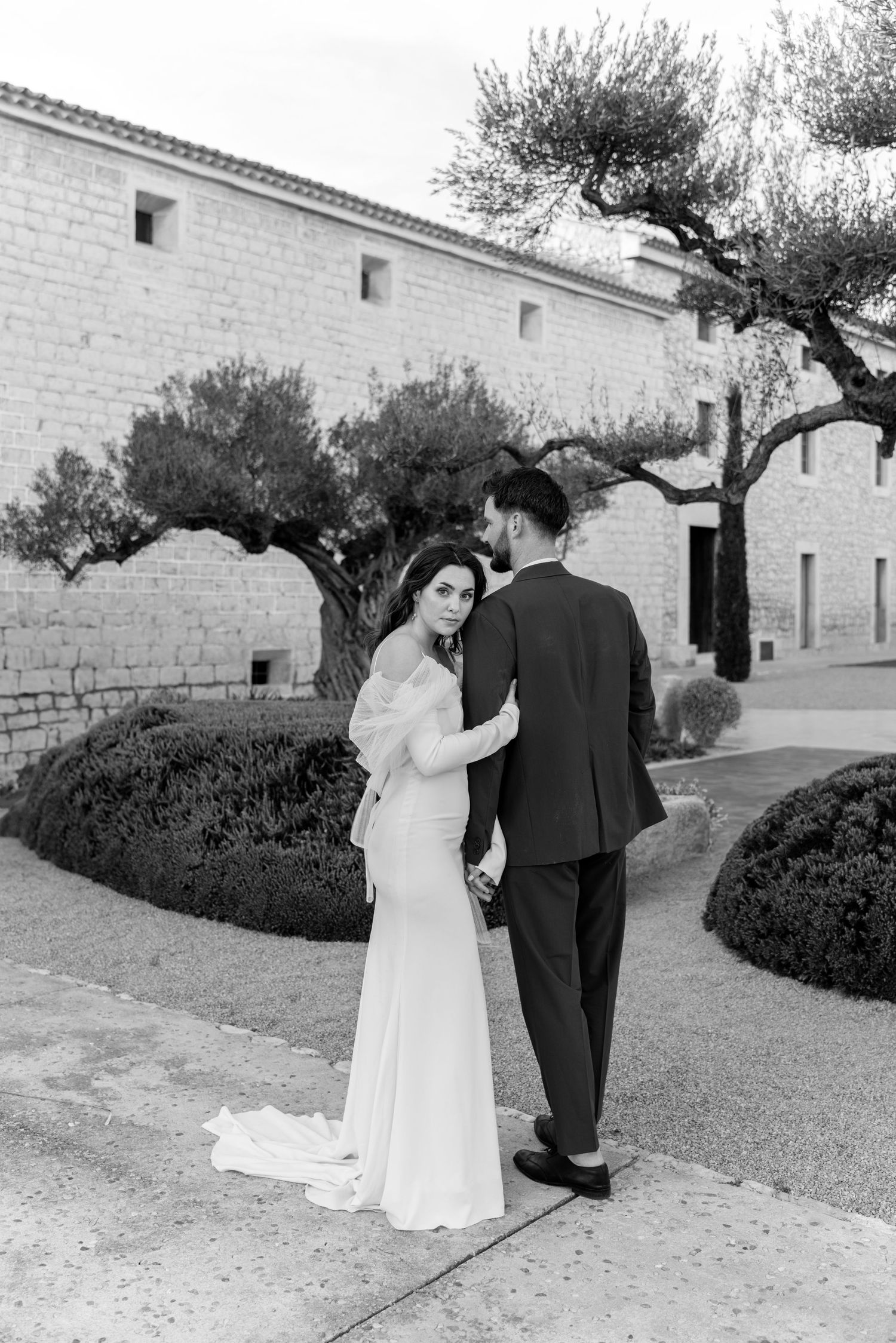 A wedding couple sharing a moment outside a traditional stone building with olive trees.