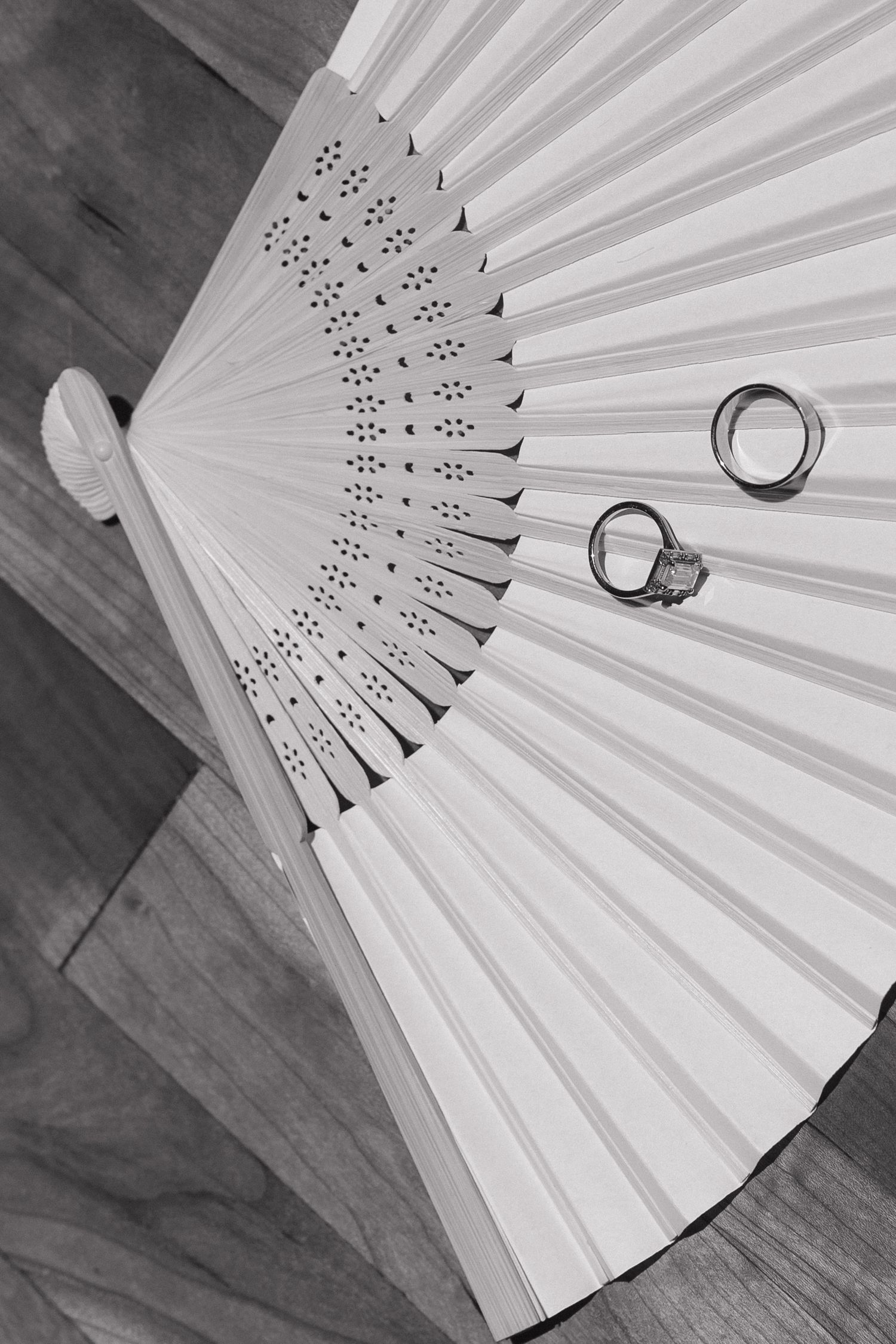 White paper fan with wedding rings artistically arranged on wooden surface.