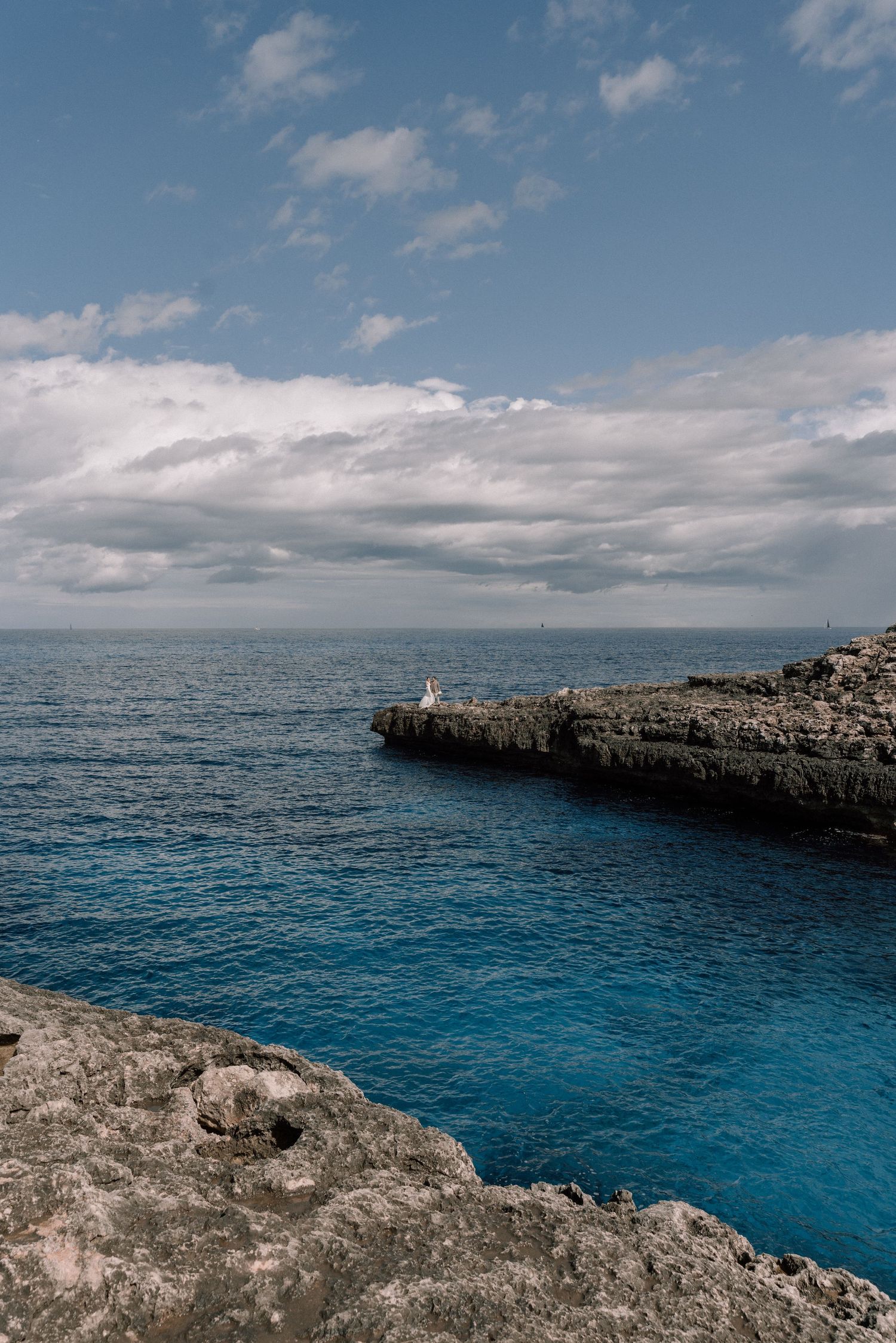 Rocky coastal cliffs overlooking deep blue Mediterranean waters under a bright summer sky.