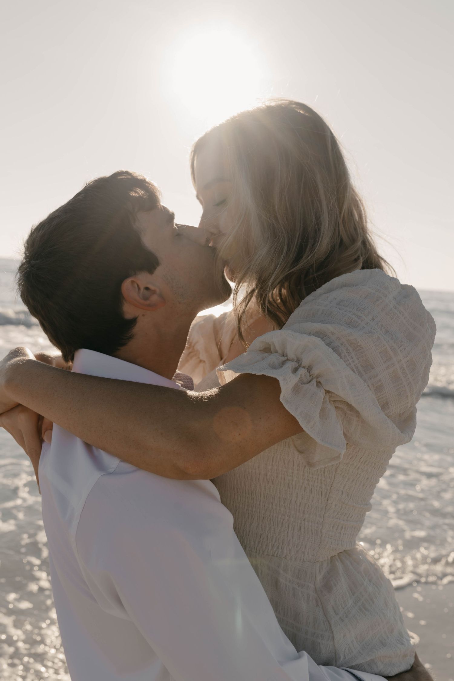 Romantic embrace captured against sparkling ocean backdrop during sunset.