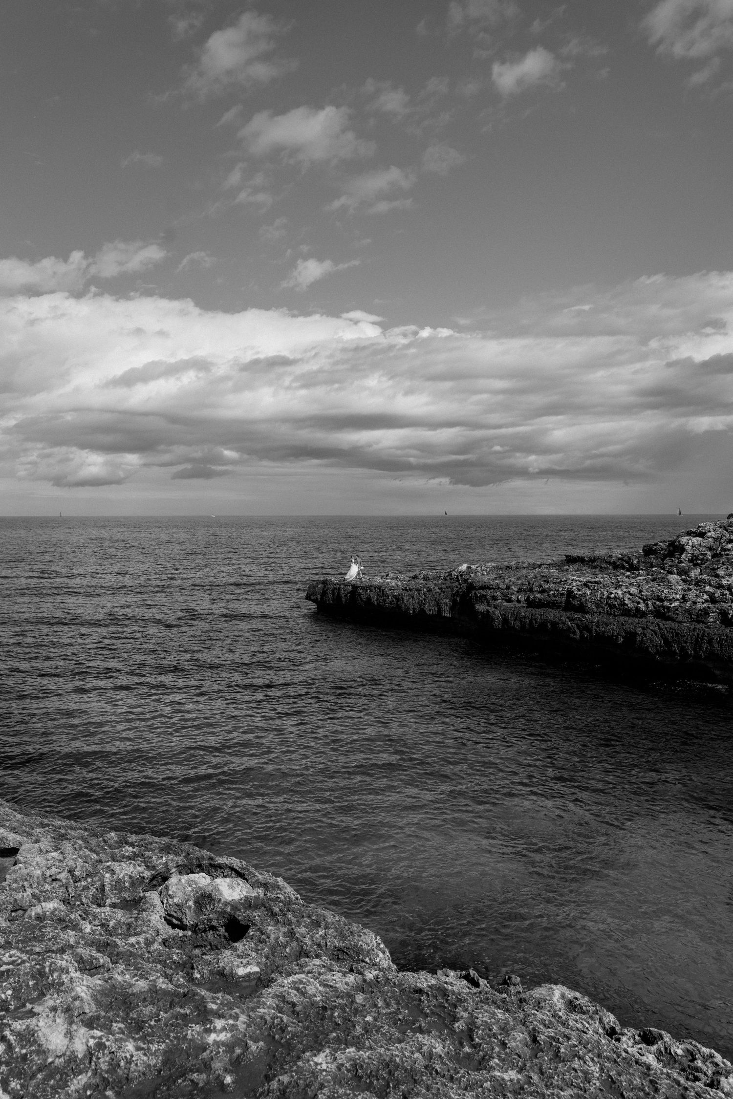 Black and white seascape with rocky coastal cliffs extending into dark ocean waters under cloudy skies.