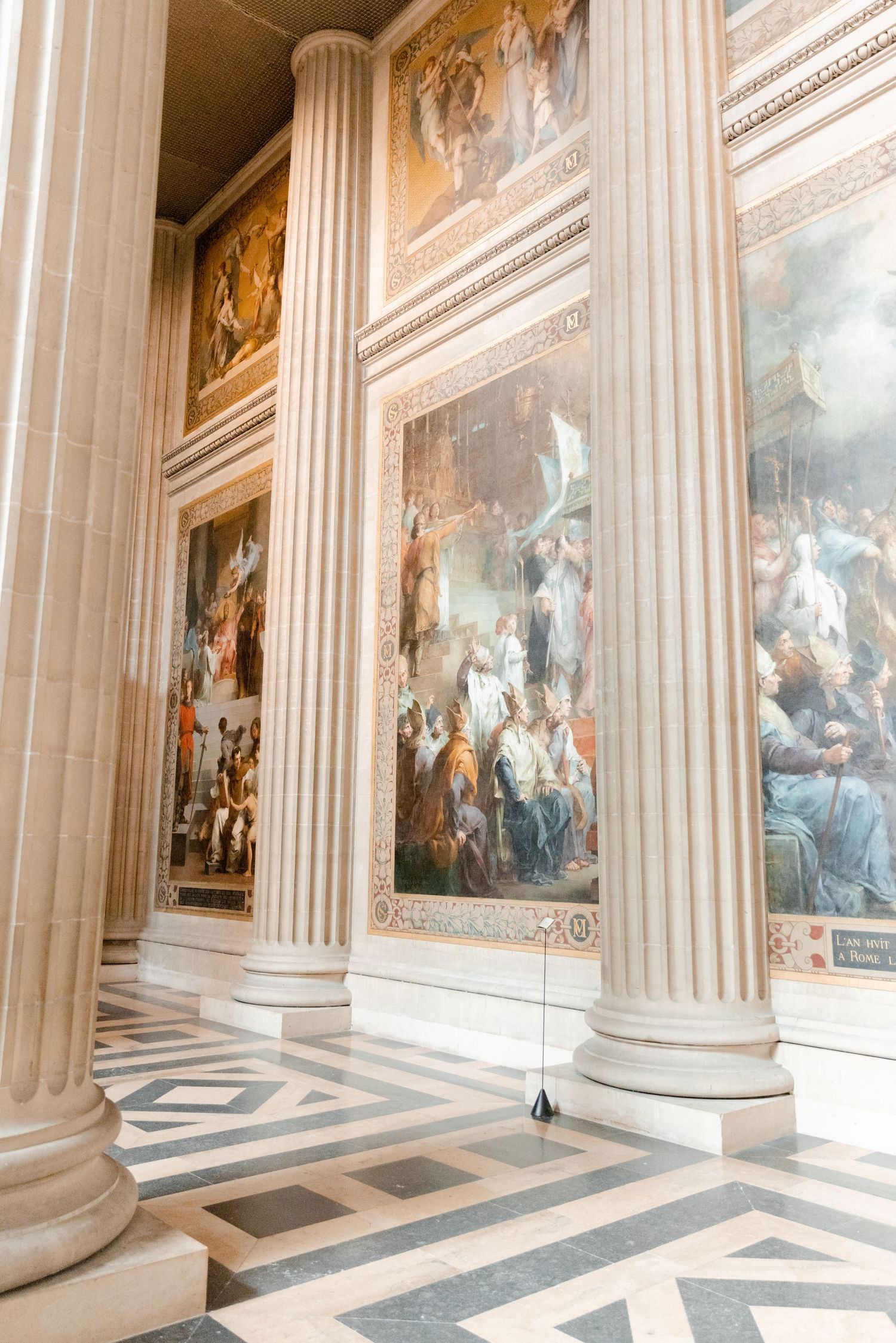 Grand hallway with classical columns and historic paintings in ornate gold frames.