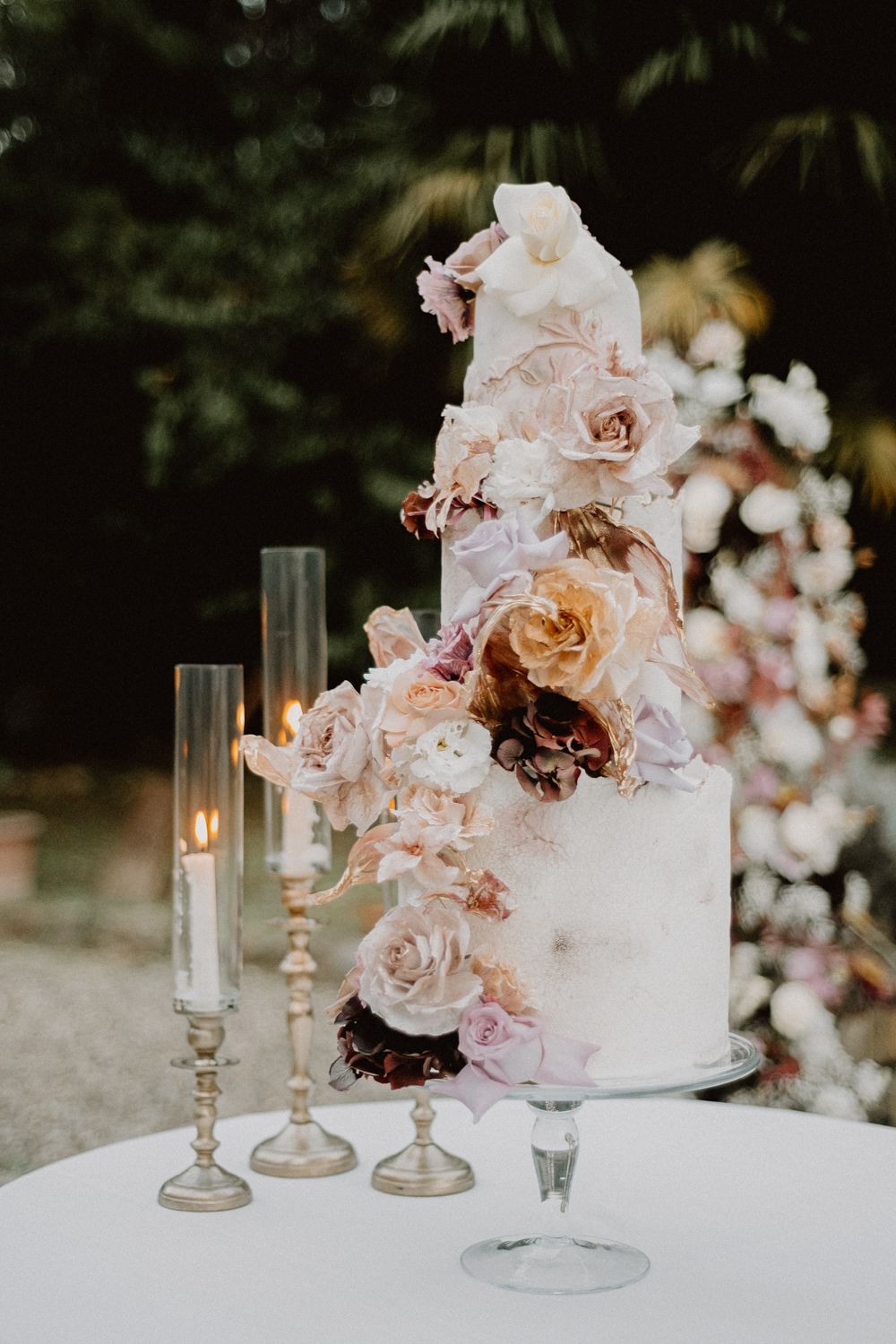 Elegant tiered white wedding cake decorated with blush roses and candle holders.