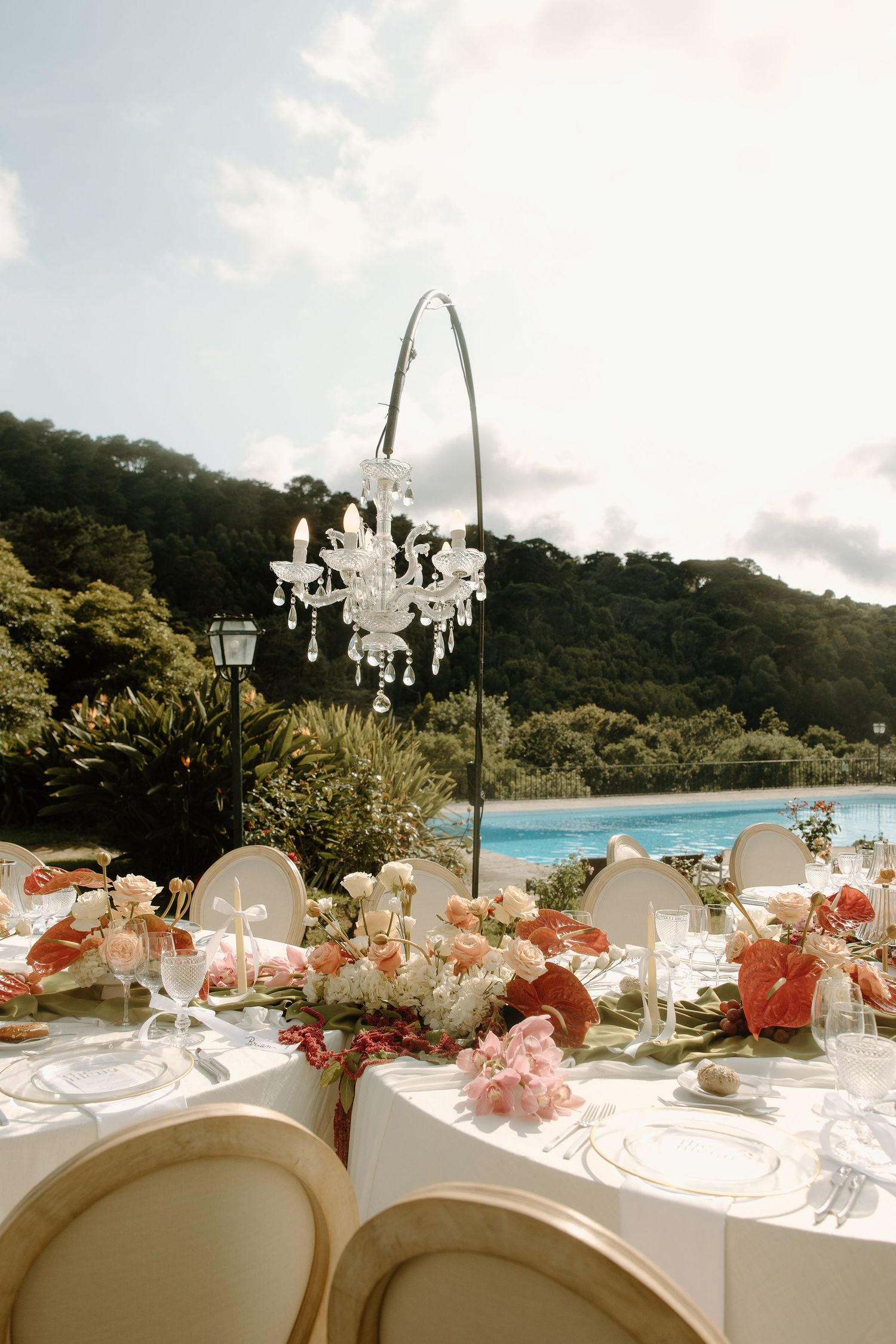 Elegant outdoor wedding reception table setting with crystal chandeliers and floral centerpieces.