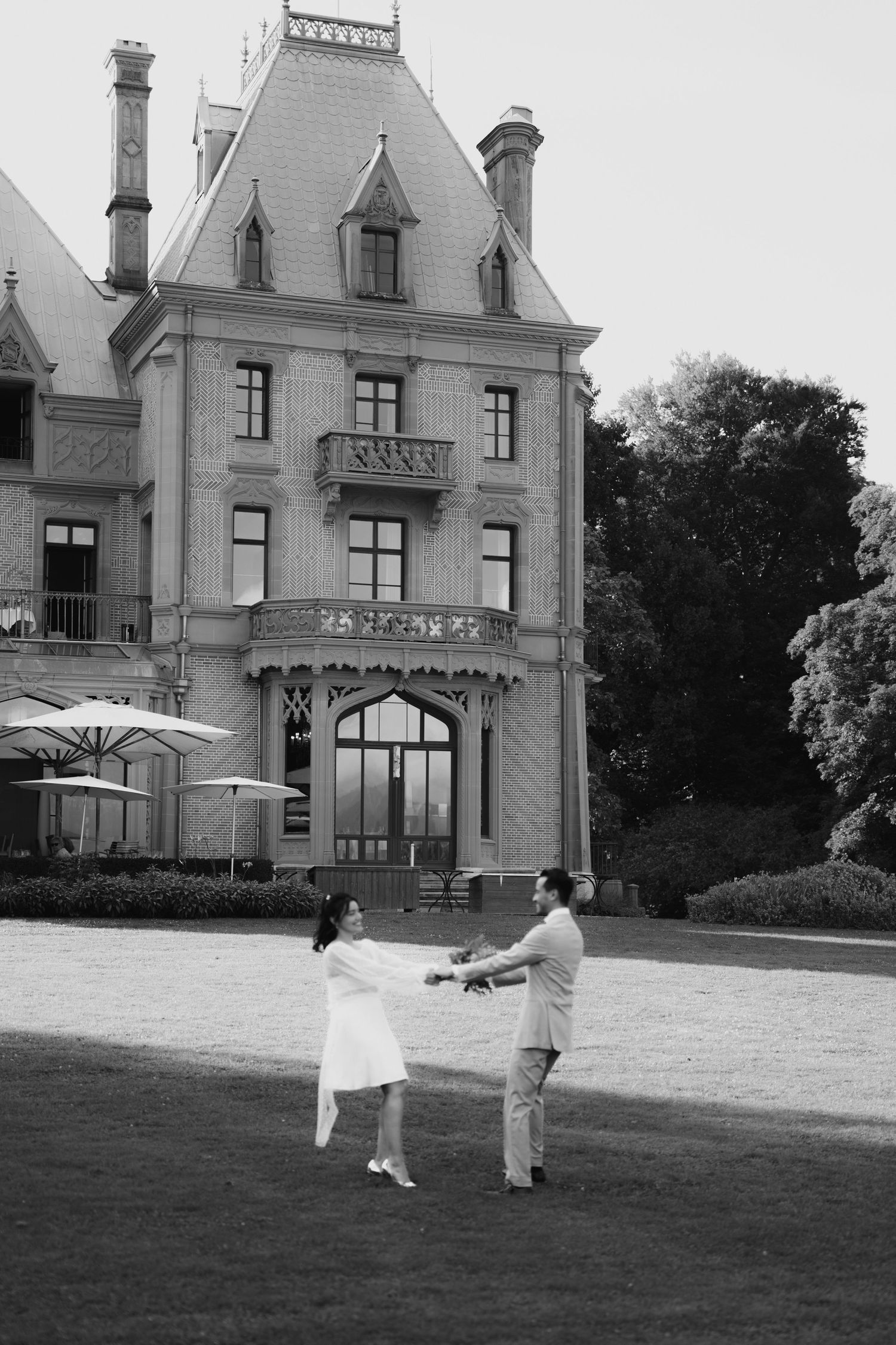 Black and white photo of couple with umbrella in front of historic mansion.