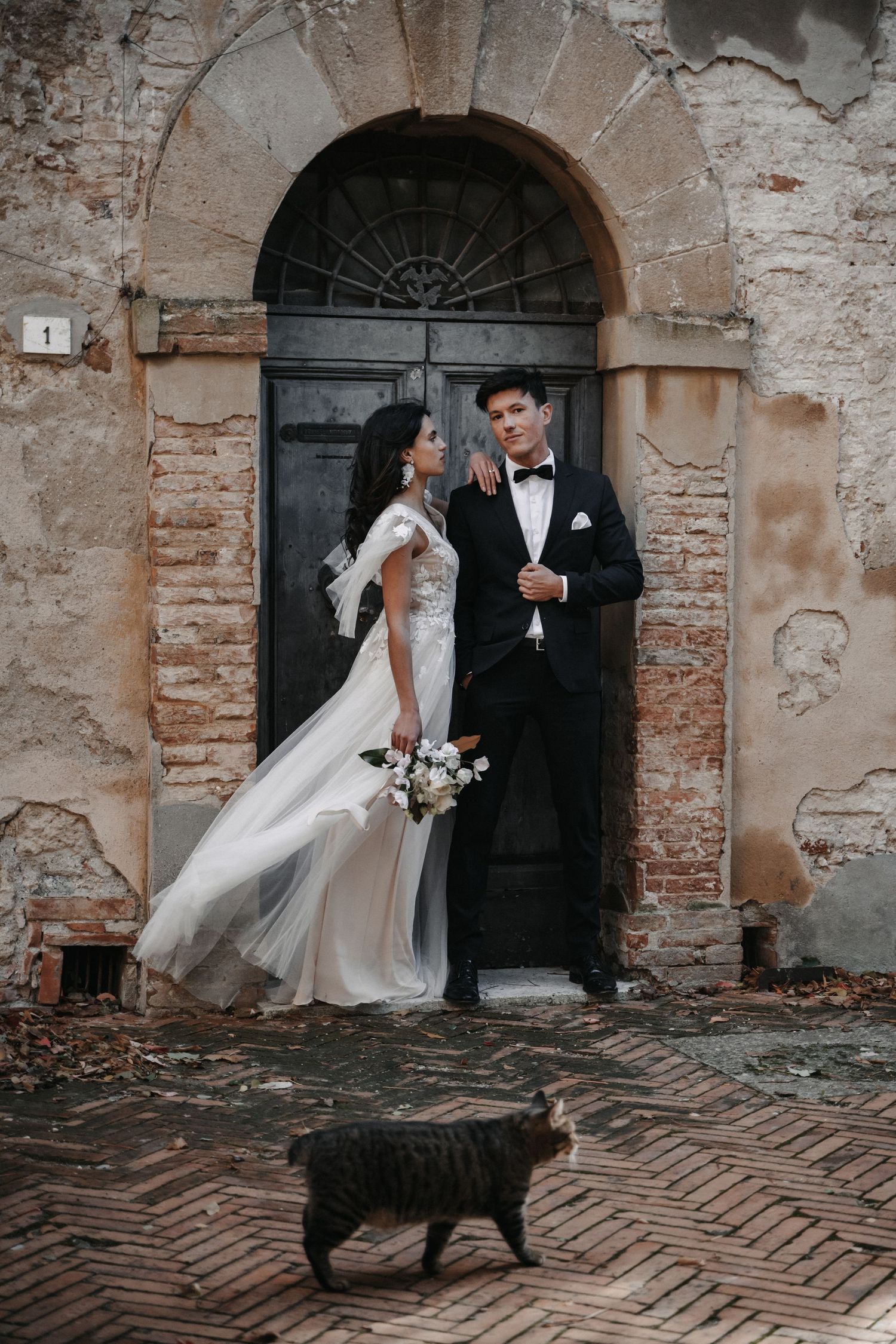A newlywed couple poses dramatically against rustic stone walls and arched doorways.
