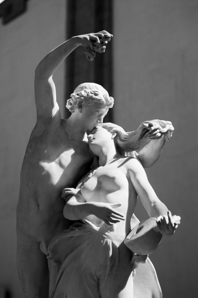 Classical stone statue depicting romantic figures in dramatic embrace captured in black and white.